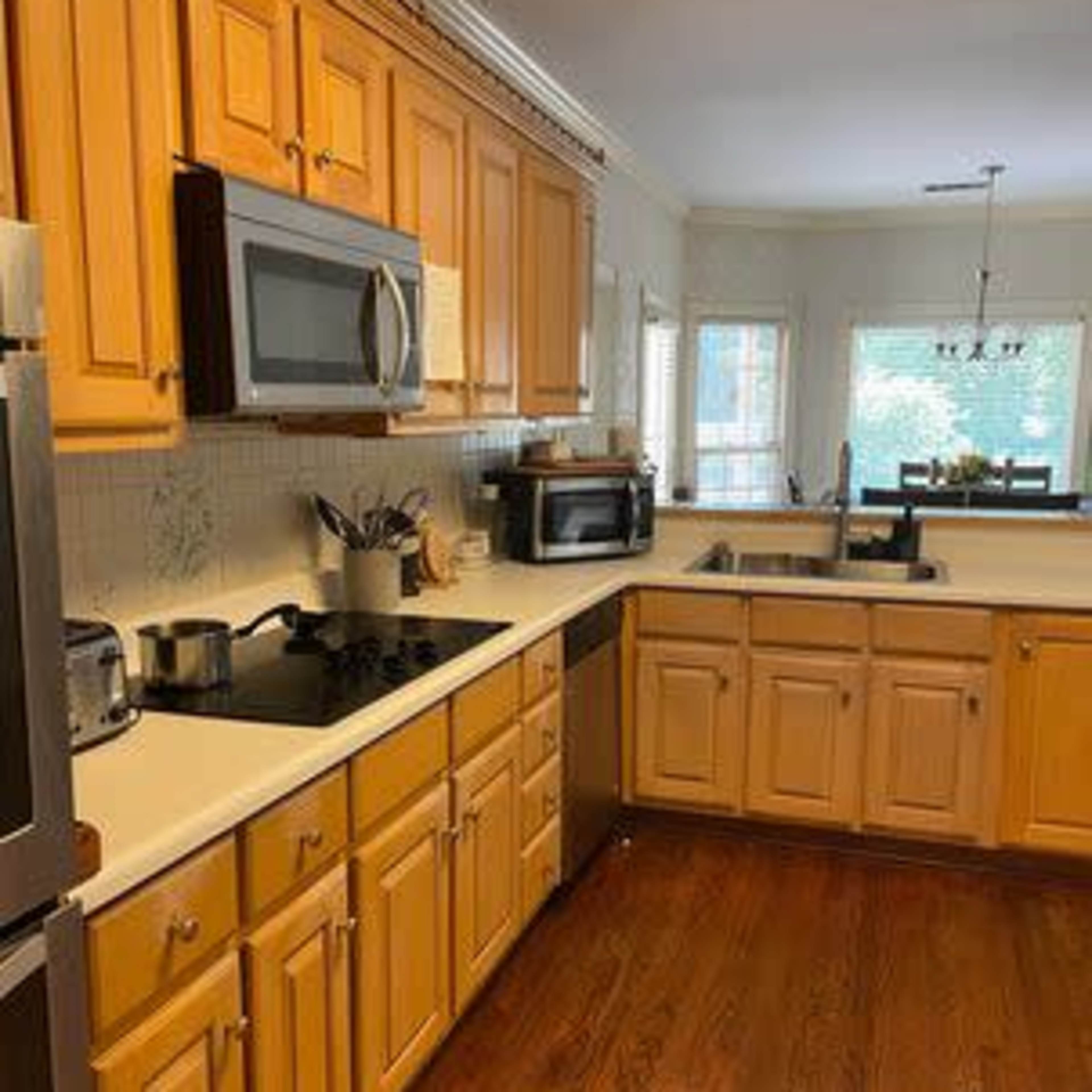 A kitchen with wooden cabinets, a stainless steel refrigerator, a microwave, and a sink, featuring a window and natural light.