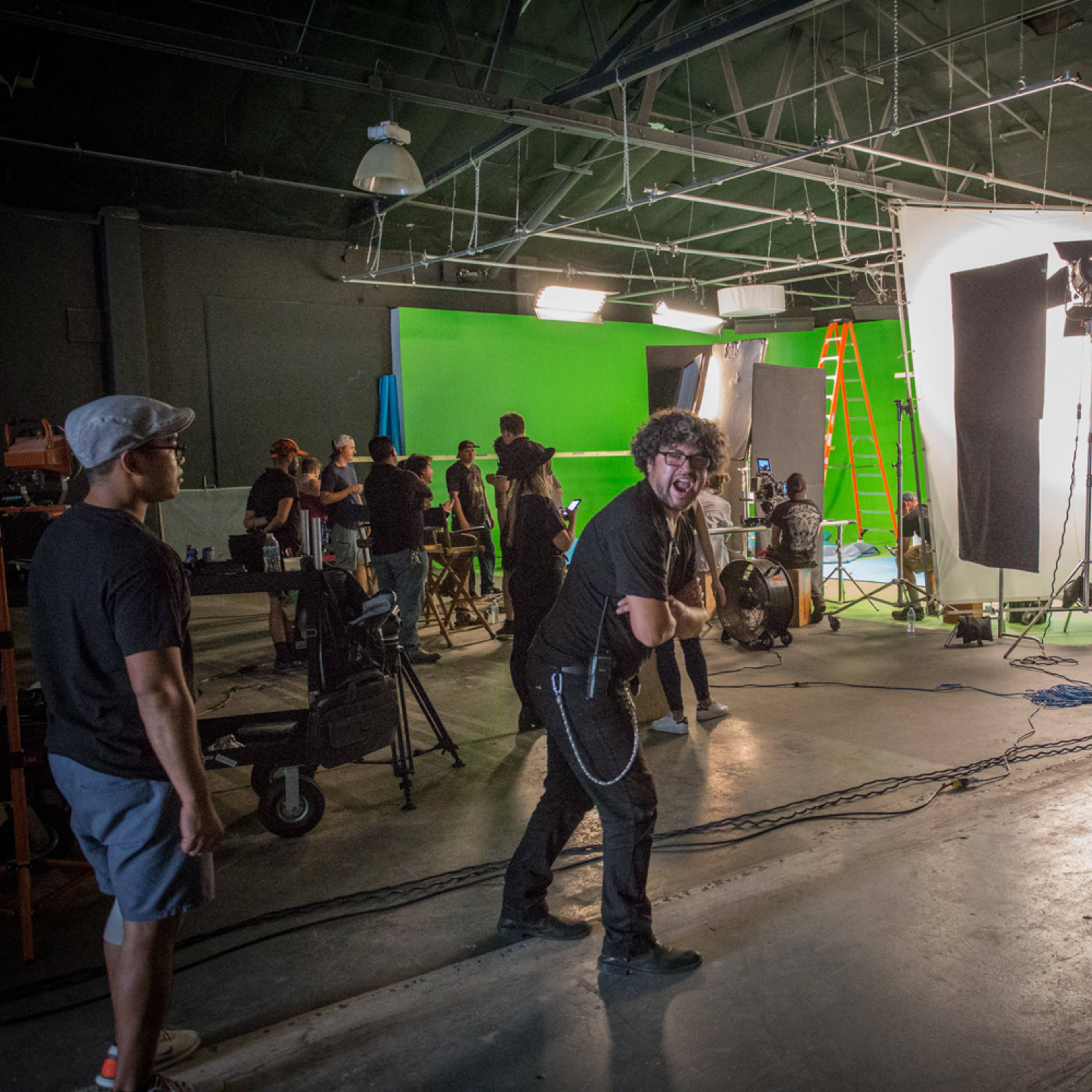 A group of people is working in a film studio with green screens and lighting equipment set up for a shoot.