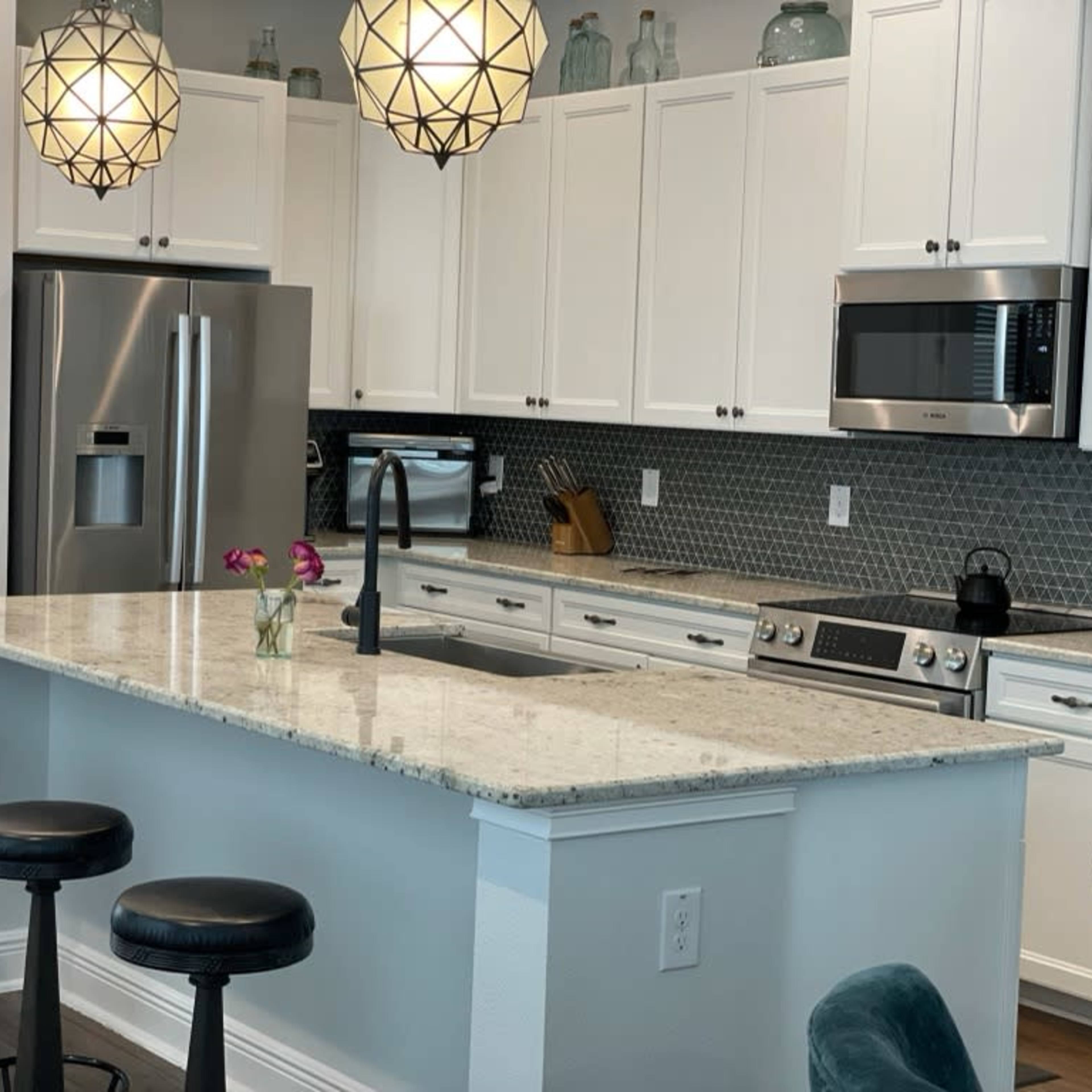 A modern kitchen with white cabinets, a marble countertop, and two pendant lights hanging above the island.