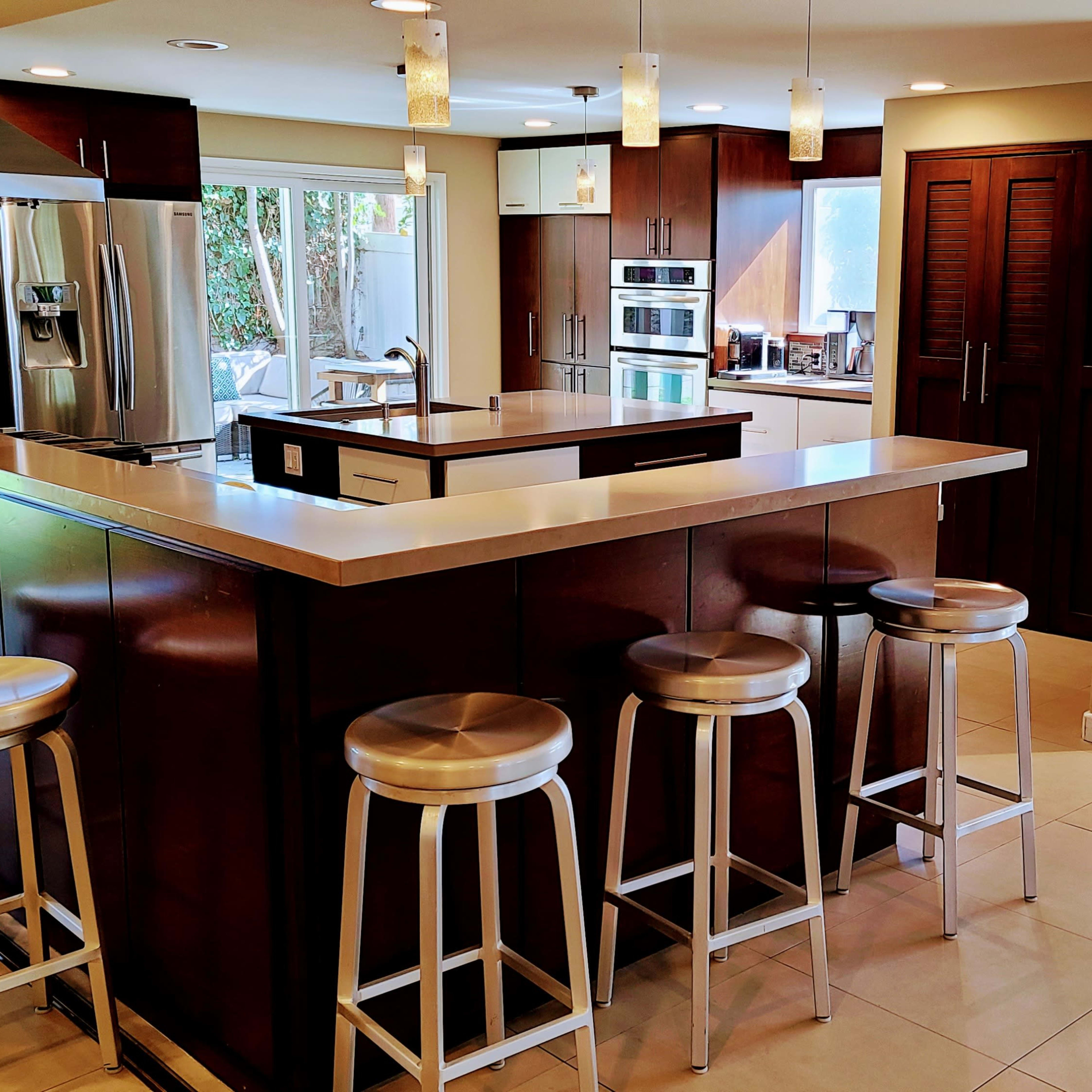 A modern kitchen with dark cabinets, a central island, and metal bar stools arranged around it.