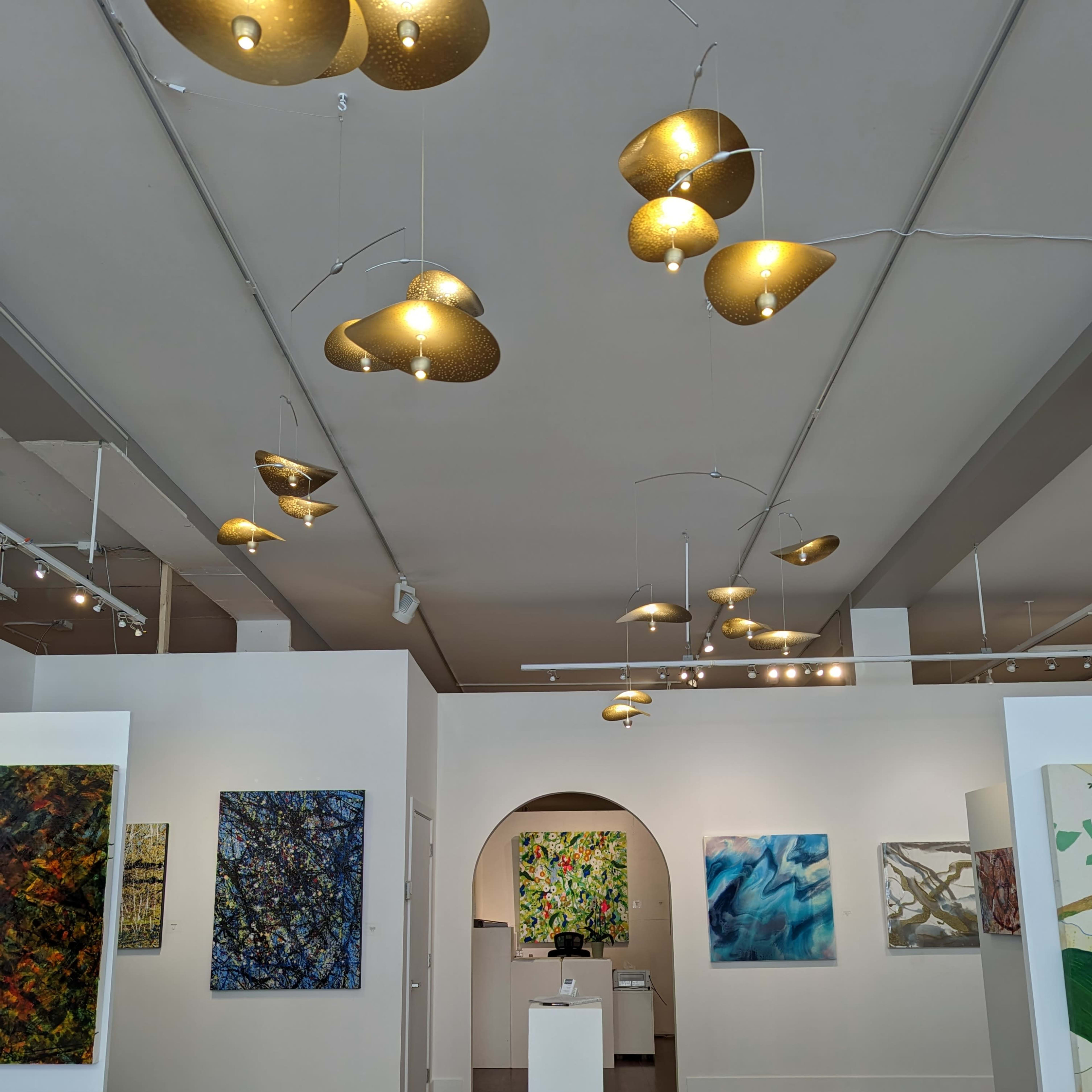 An art gallery featuring several colorful paintings on the walls and hanging light fixtures above.