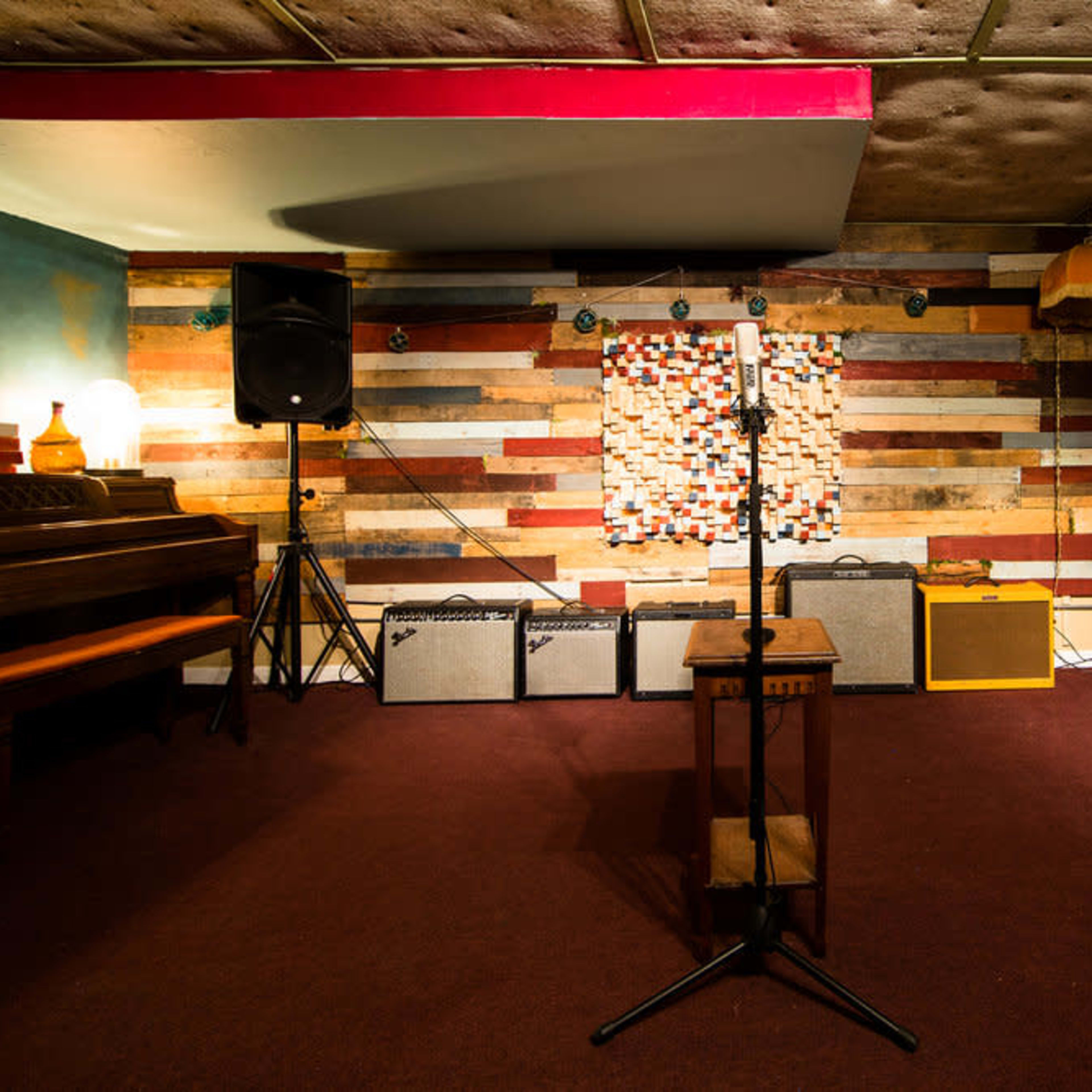 A music performance space featuring a microphone stand in front of amplifiers and a colorful wooden wall.