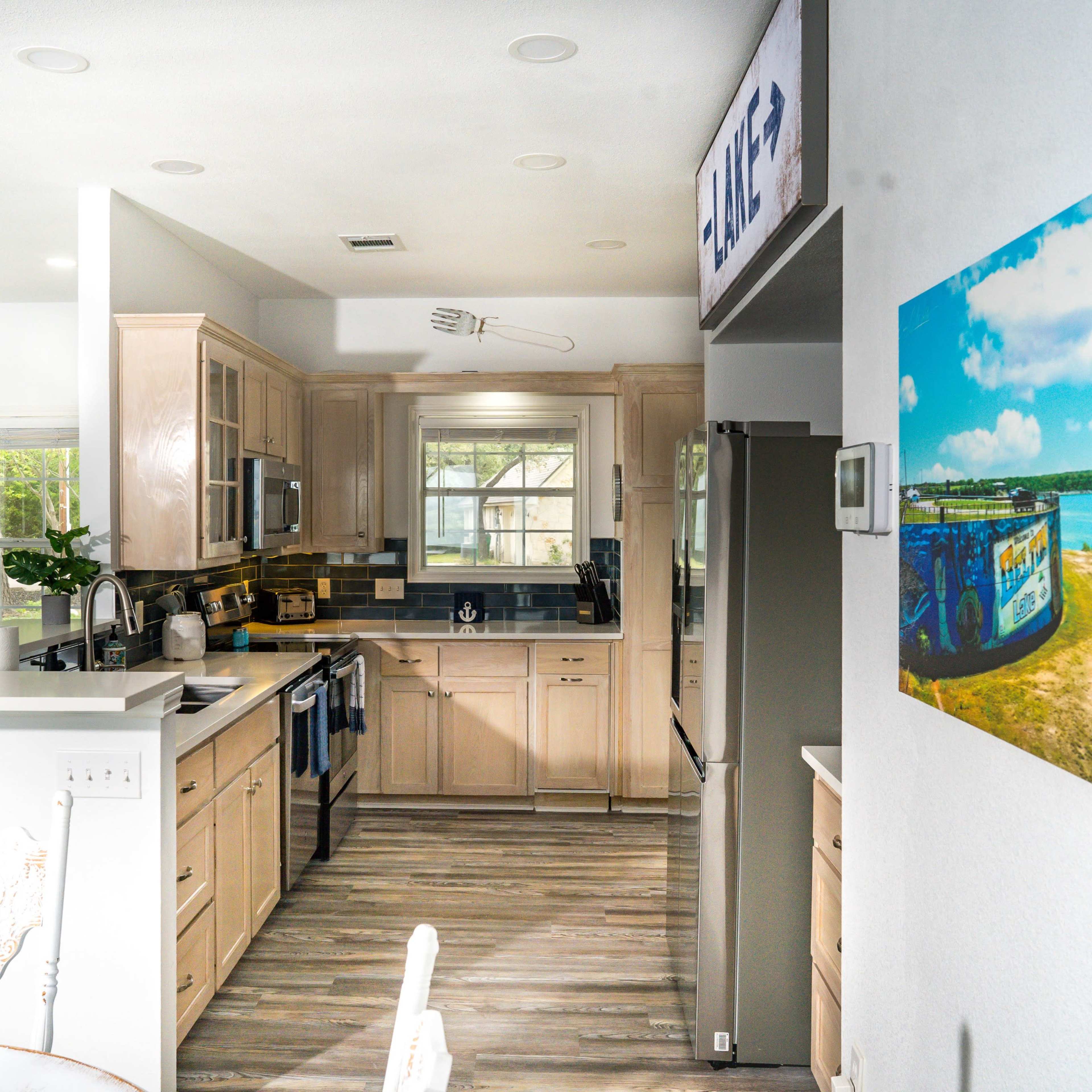 A modern kitchen features light wood cabinetry, stainless steel appliances, and an open layout with a dining area.
