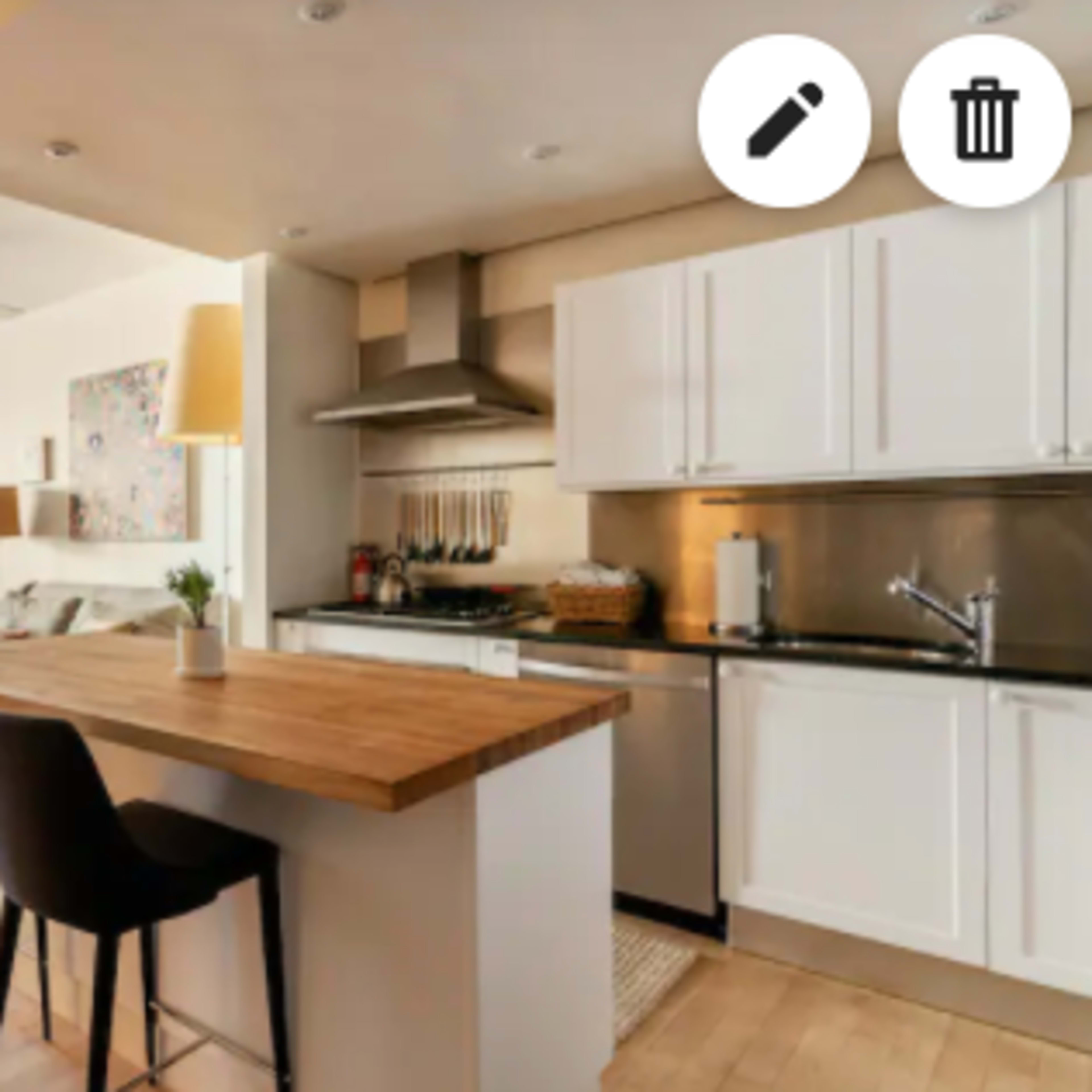 A modern kitchen with a wooden island and bar stools opens up to a dining area featuring a table and chairs.
