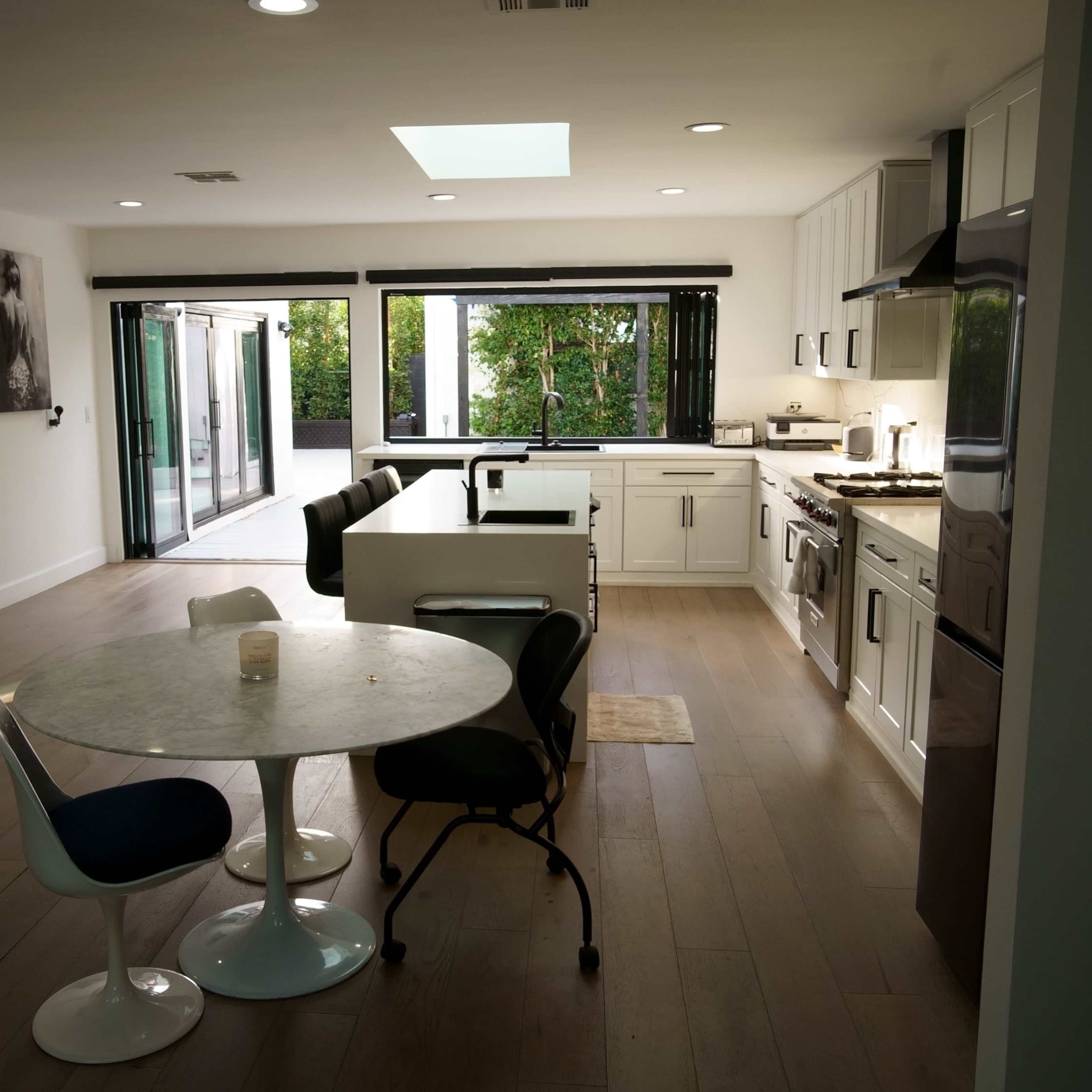A modern kitchen and dining area feature white cabinetry, a marble table, and large glass doors leading to an outdoor space.