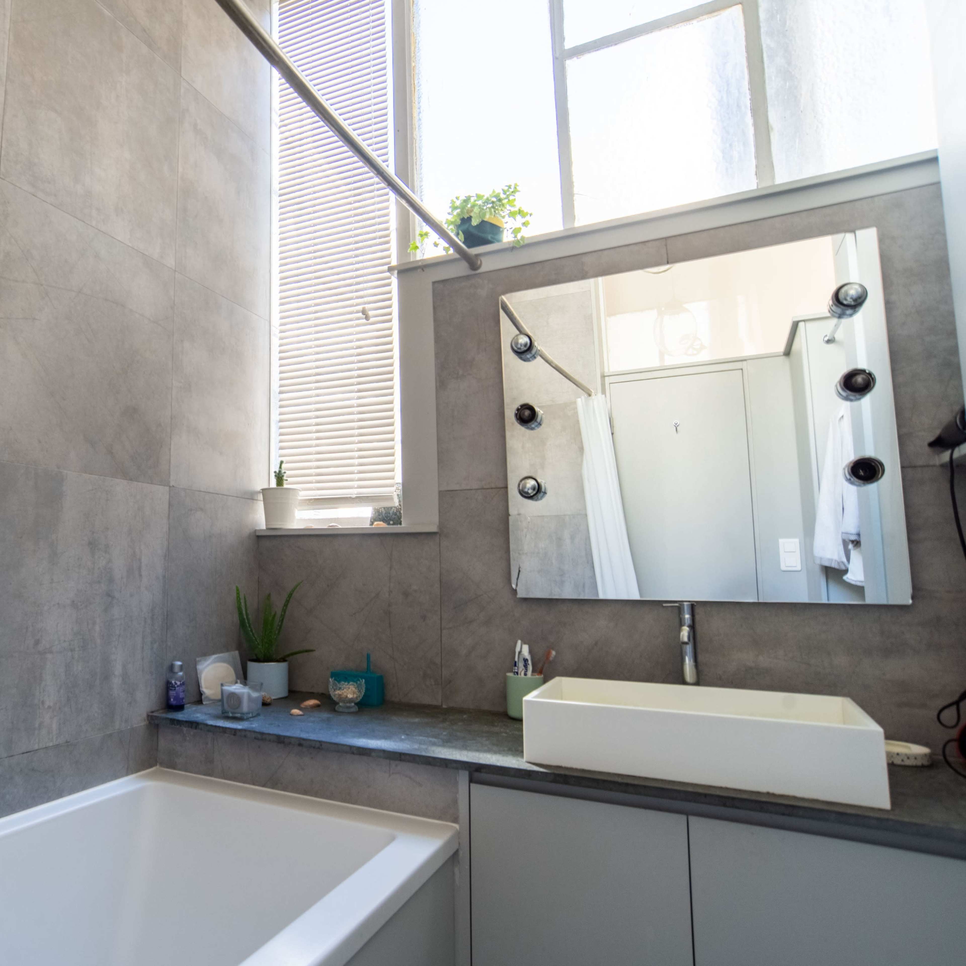 A modern bathroom featuring a bathtub, a wall-mounted showerhead, a sink with a rectangular basin, and a large mirror above the sink.