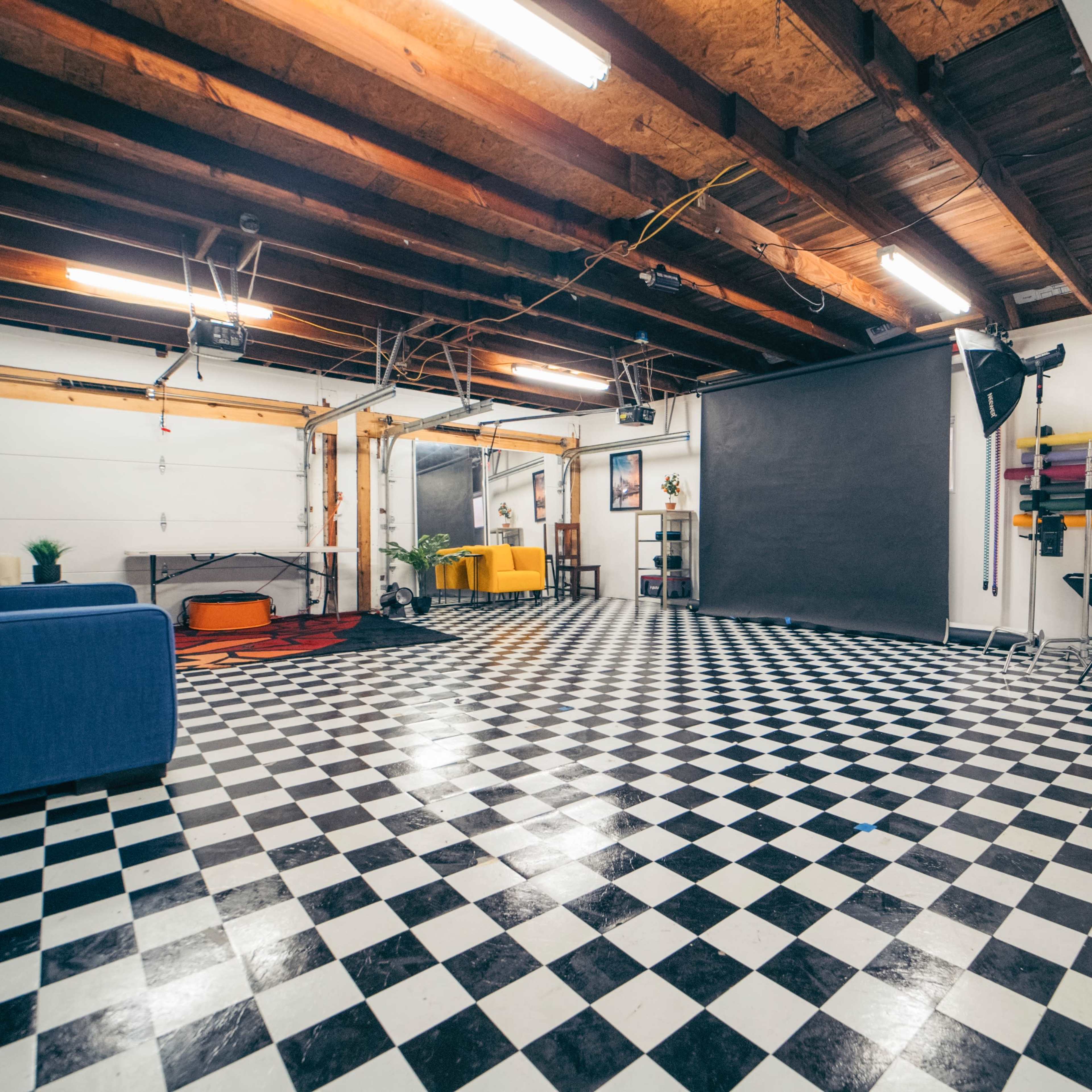 A spacious garage with a black and white checkered floor, overhead lights, and minimal furnishings.