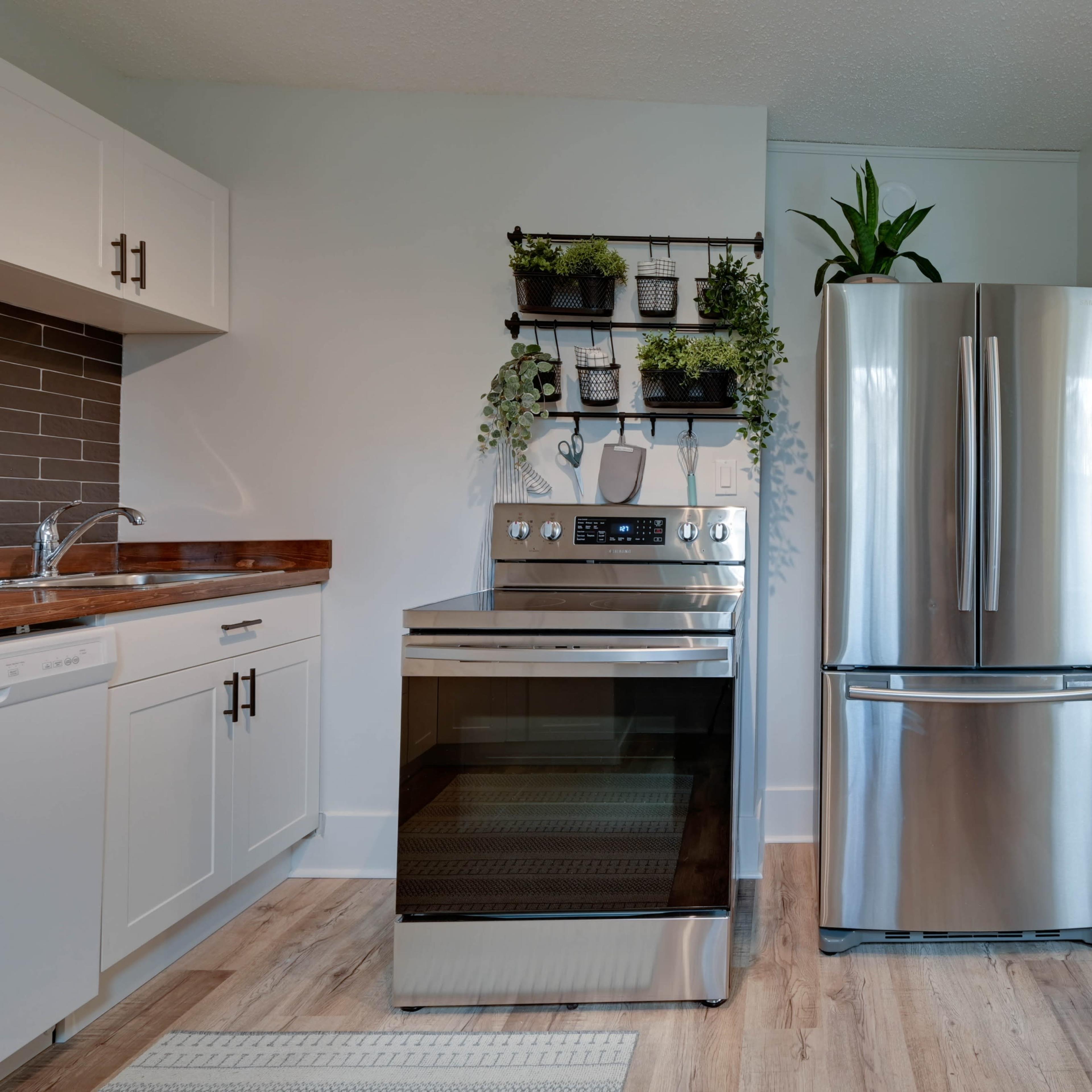 A modern kitchen featuring a stainless steel refrigerator and an oven next to a wall-mounted plant shelf.