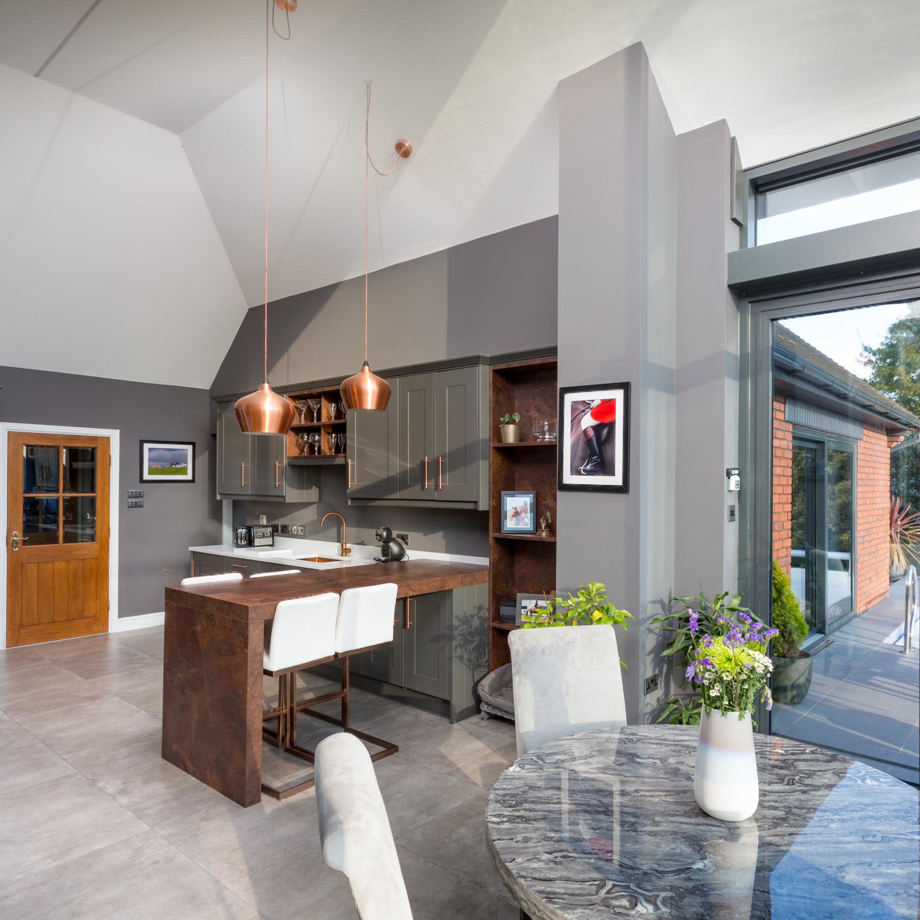 A modern kitchen and dining area featuring a dark gray color scheme, a large window, and a round table surrounded by light-colored chairs.