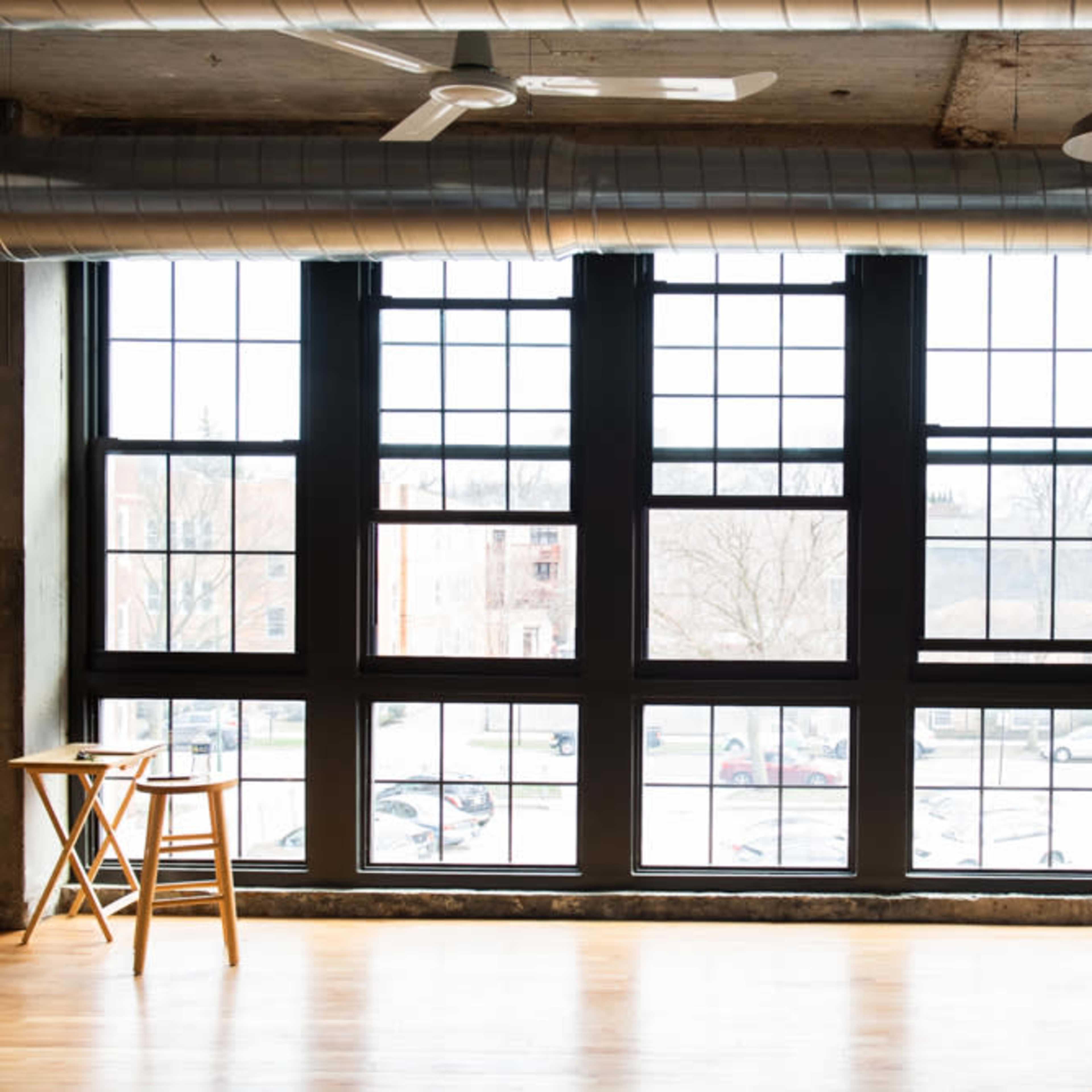 An industrial-style room with large windows, a wooden floor, a ladder, and a small table.