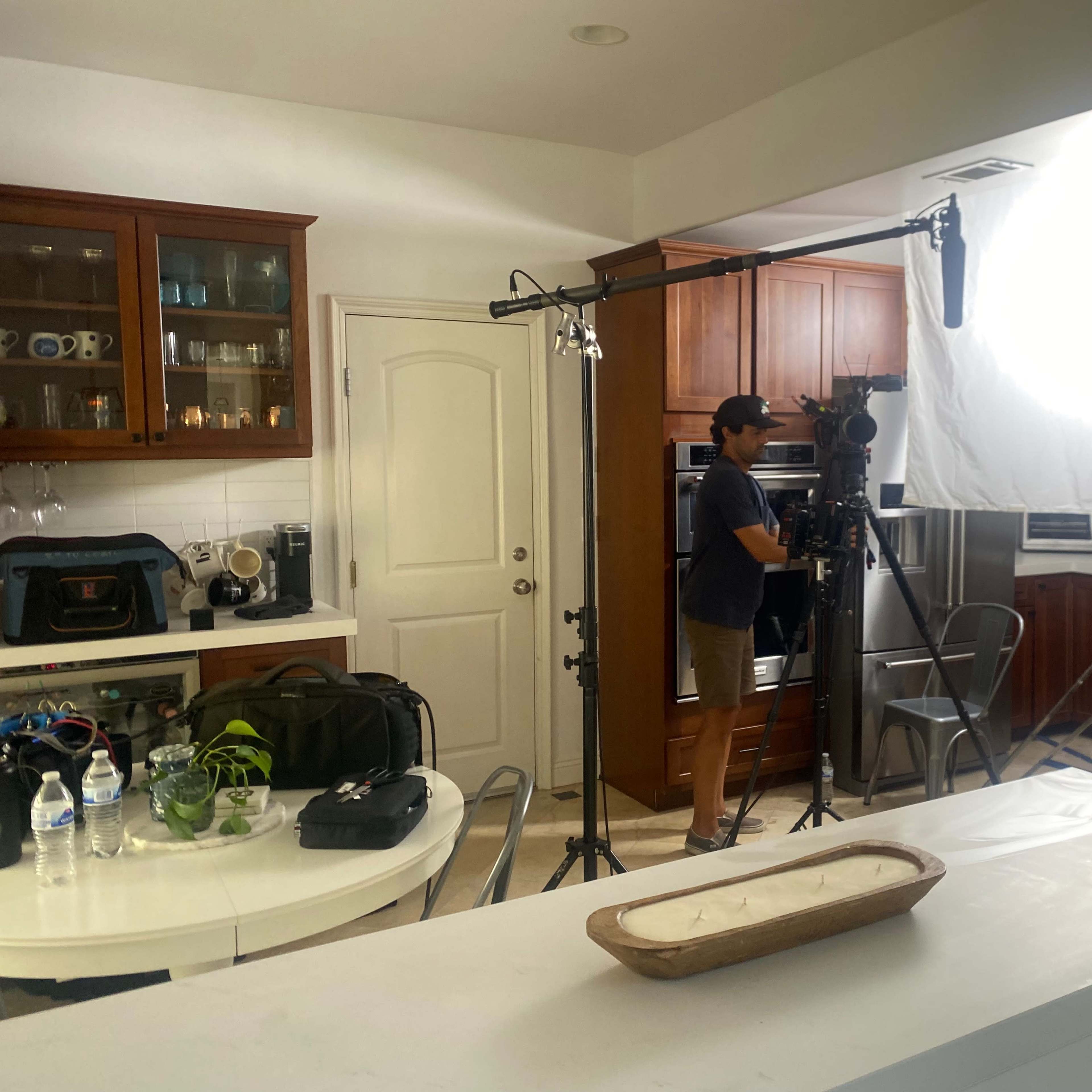 A person operates a camera setup in a kitchen equipped with wooden cabinets and professional lighting.
