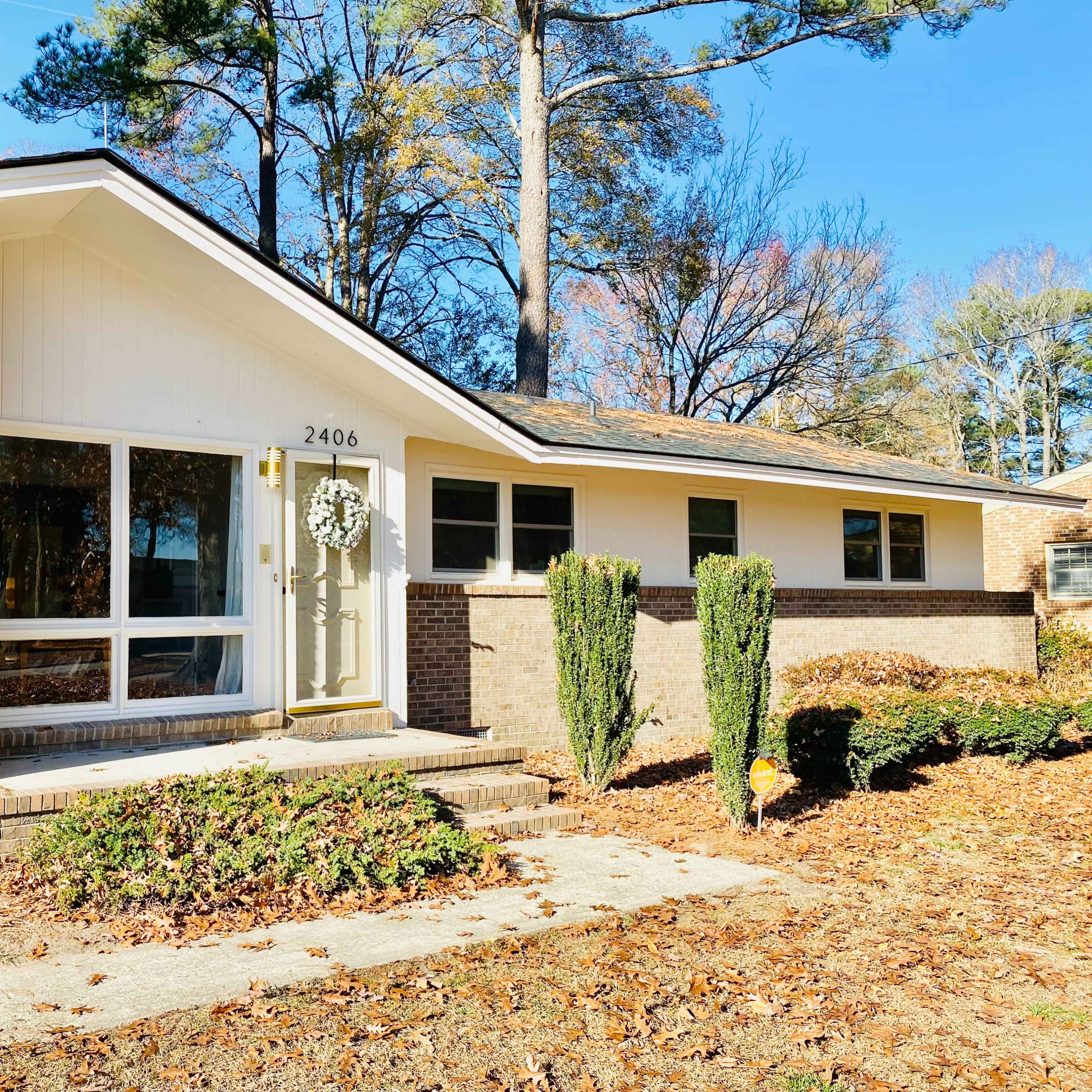A single-story house with a brick facade and a front porch, surrounded by trees and autumn foliage.