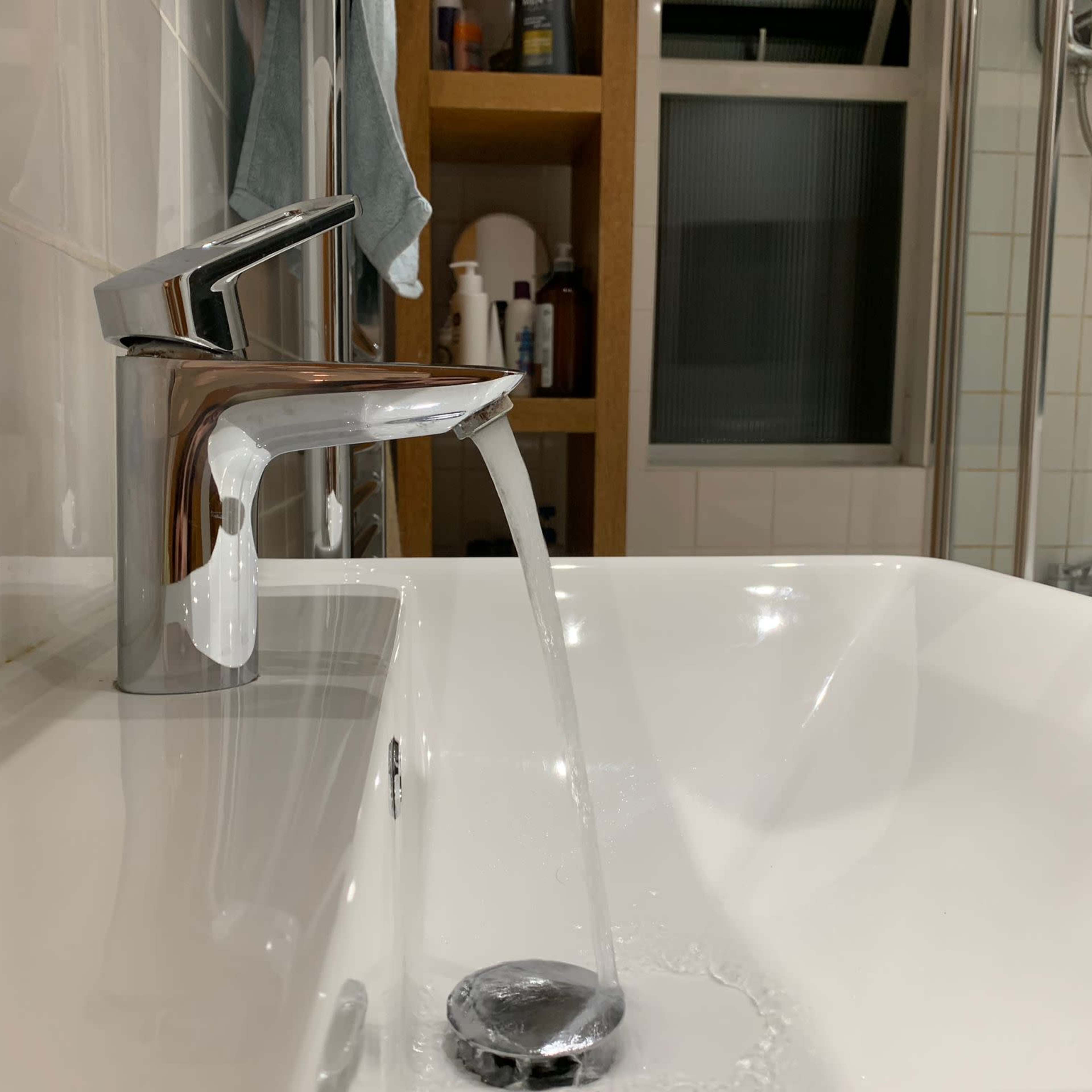A modern faucet pours water into a white bathtub in a bathroom setting.