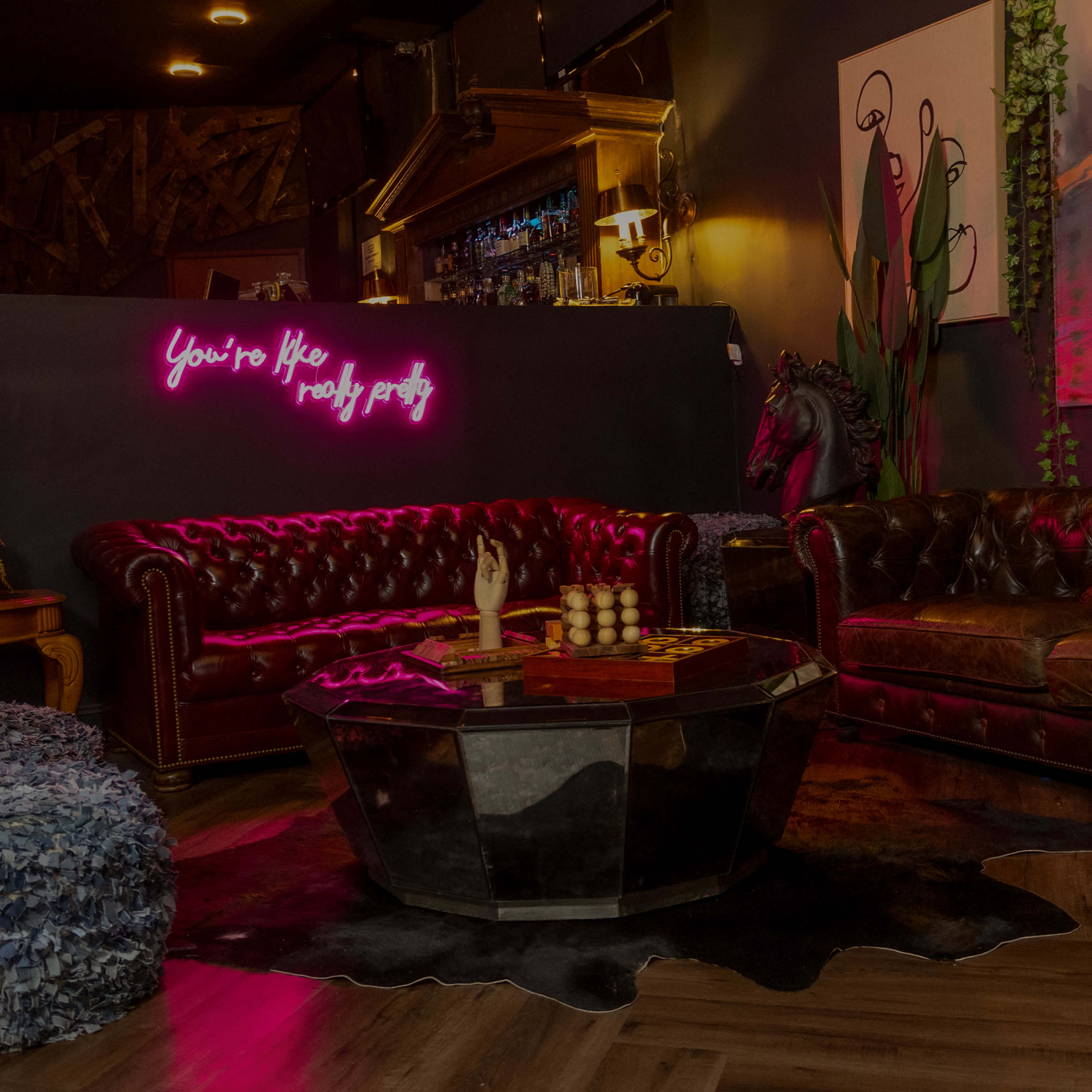 A cozy lounge area features a leather sofa, a wooden coffee table, and neon lighting on the wall.