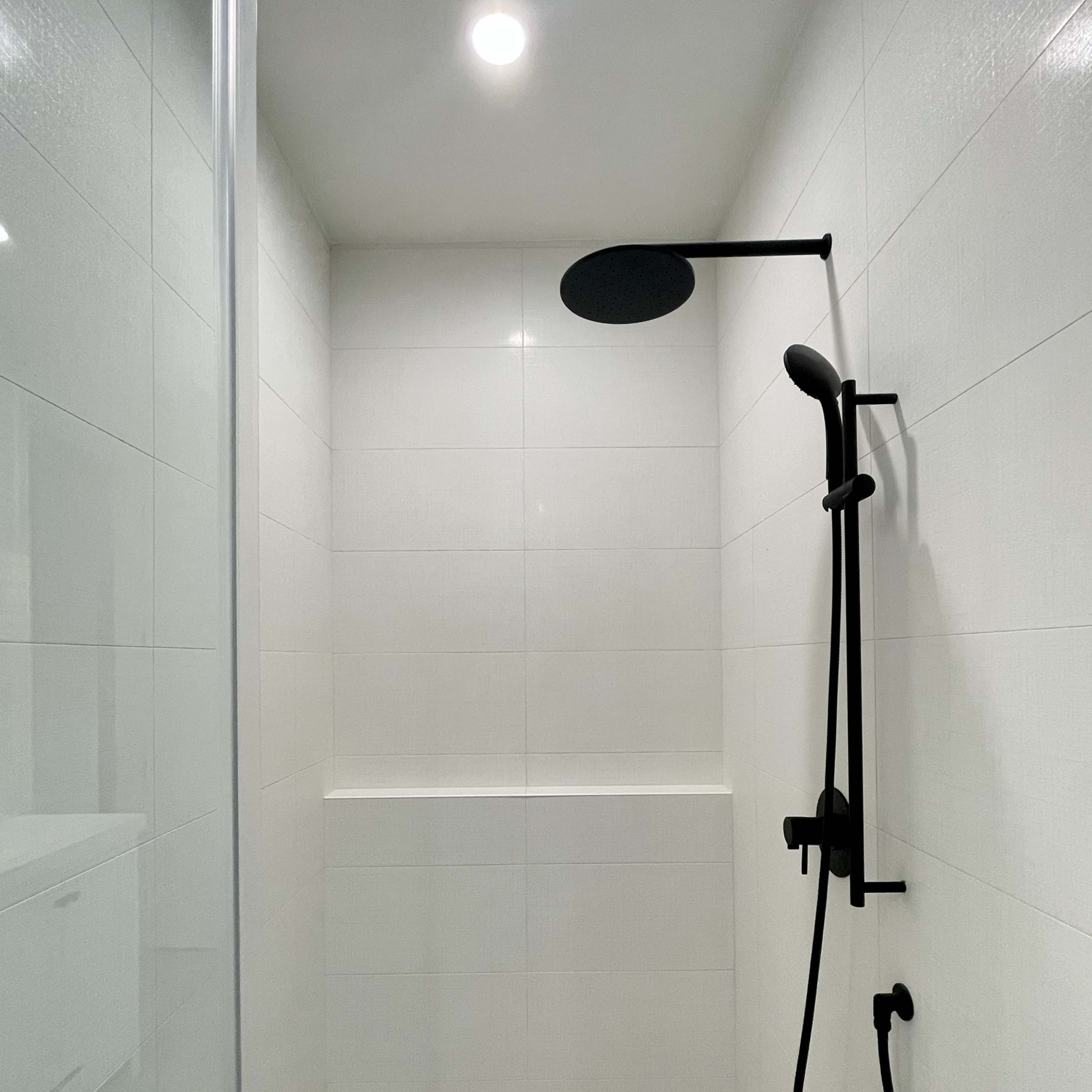 A modern shower space with a black showerhead and faucet set against white tiled walls.