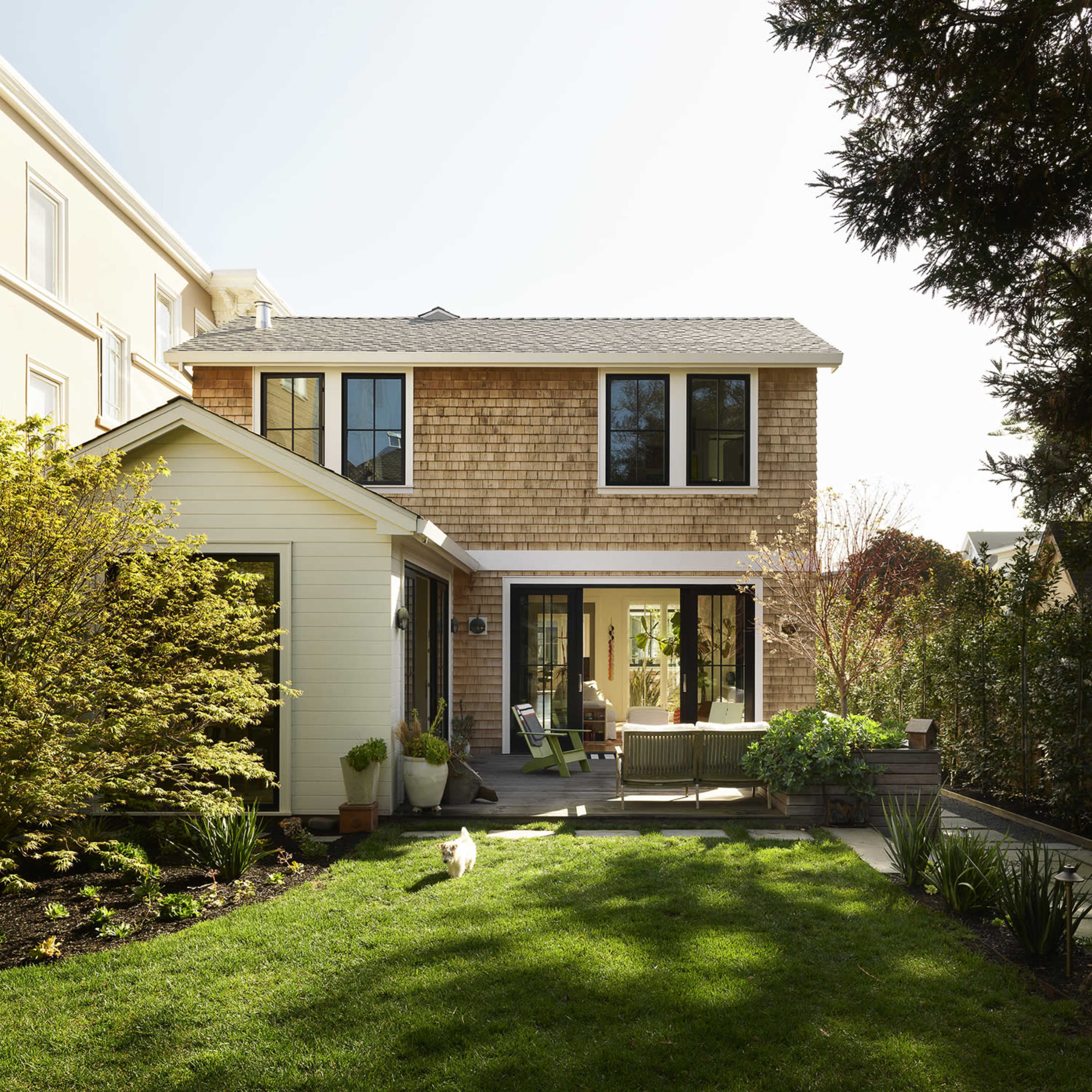 A two-story house with a shingle exterior and large windows, surrounded by a well-maintained lawn and garden.
