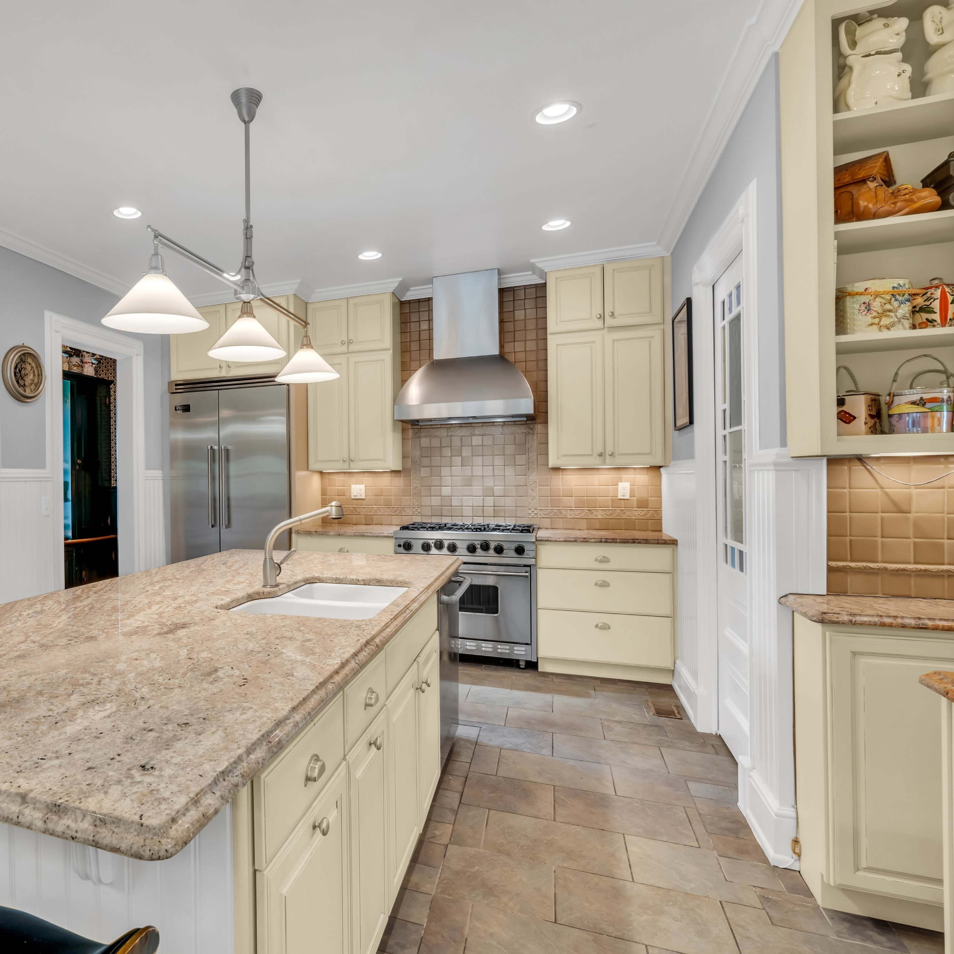 A modern kitchen features a large island with a sink, stainless steel appliances, and light-colored cabinetry.