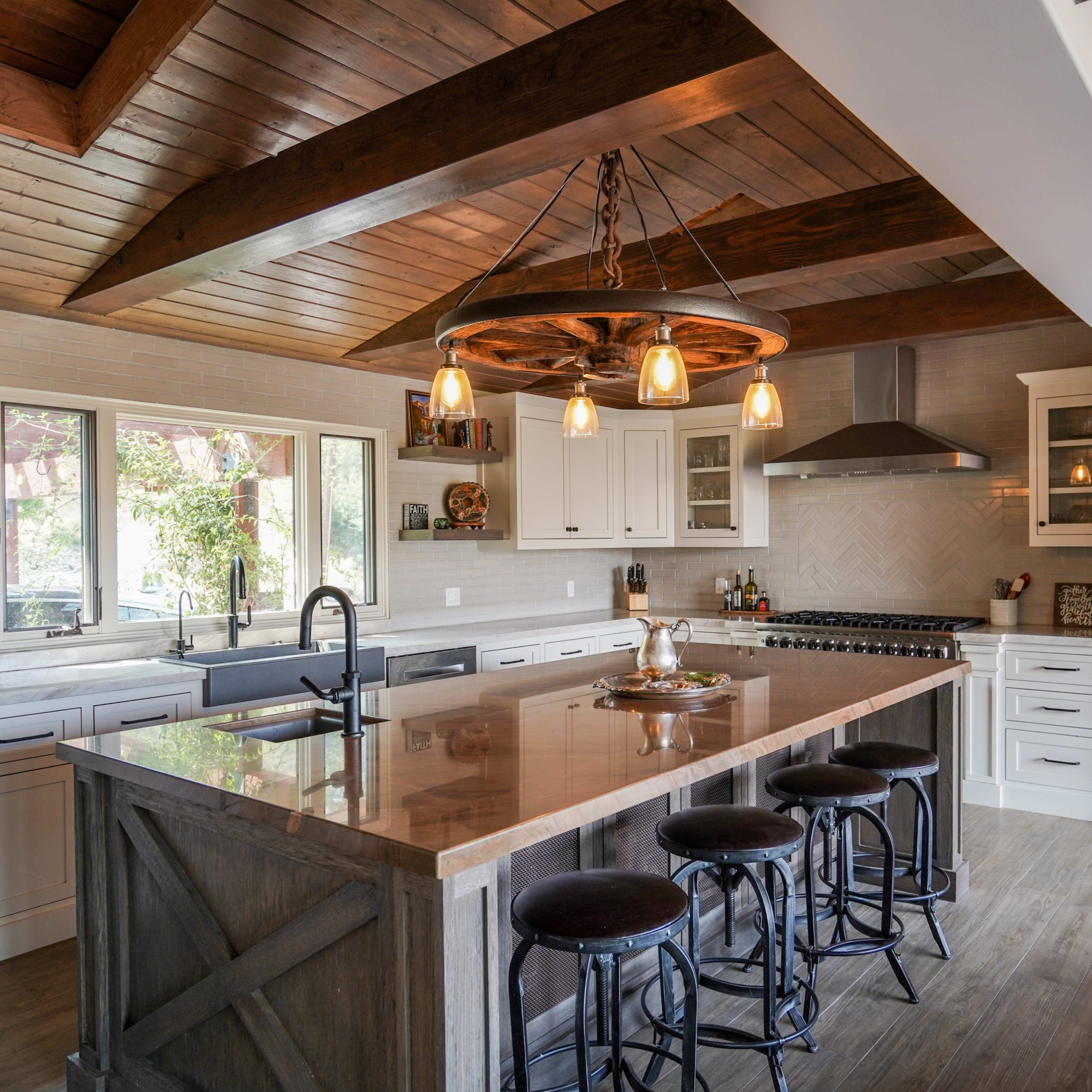 A modern kitchen featuring an island with bar stools, white cabinetry, and wooden beams overhead.