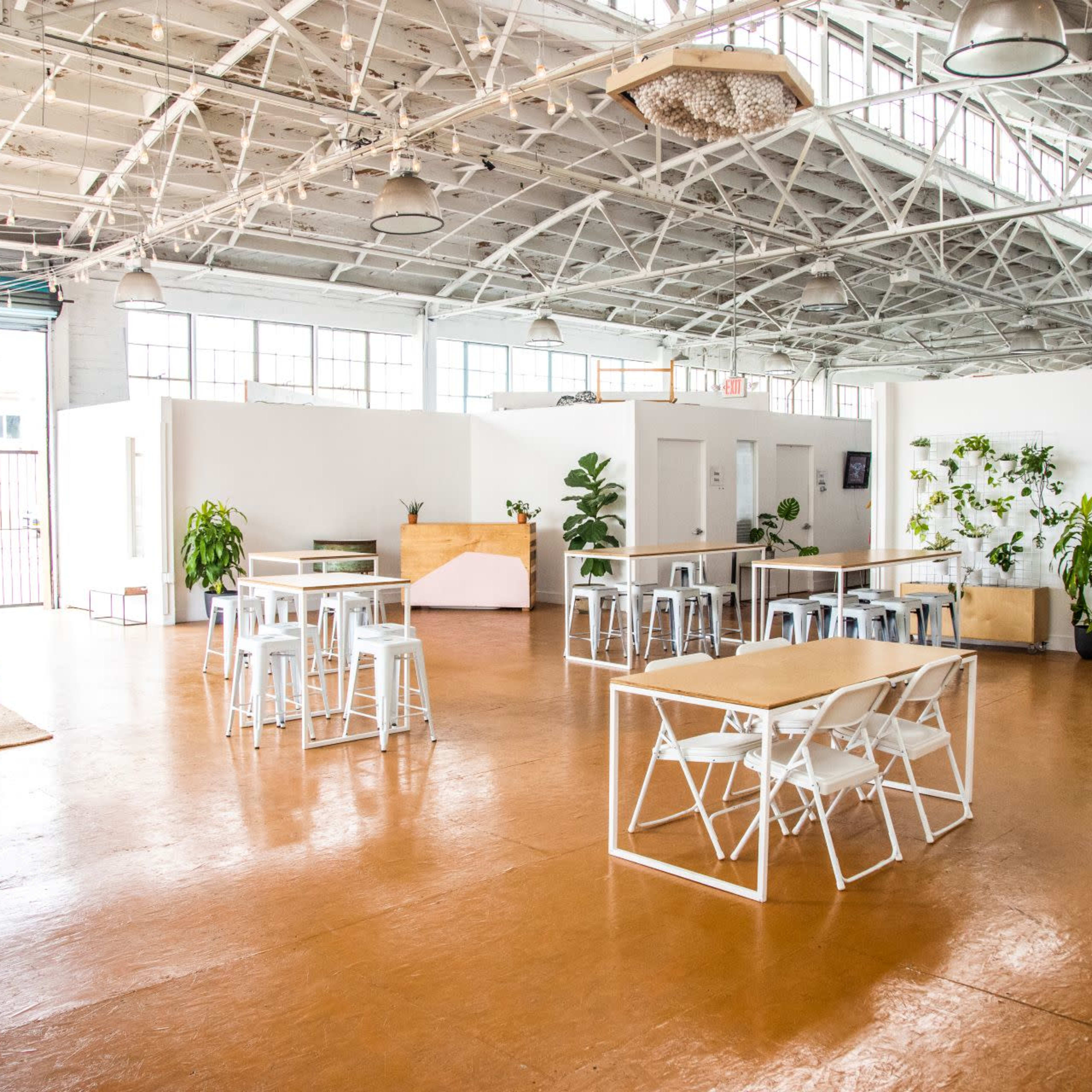 A spacious, well-lit indoor area with wooden floors, several tables and chairs, and a few plants placed around.