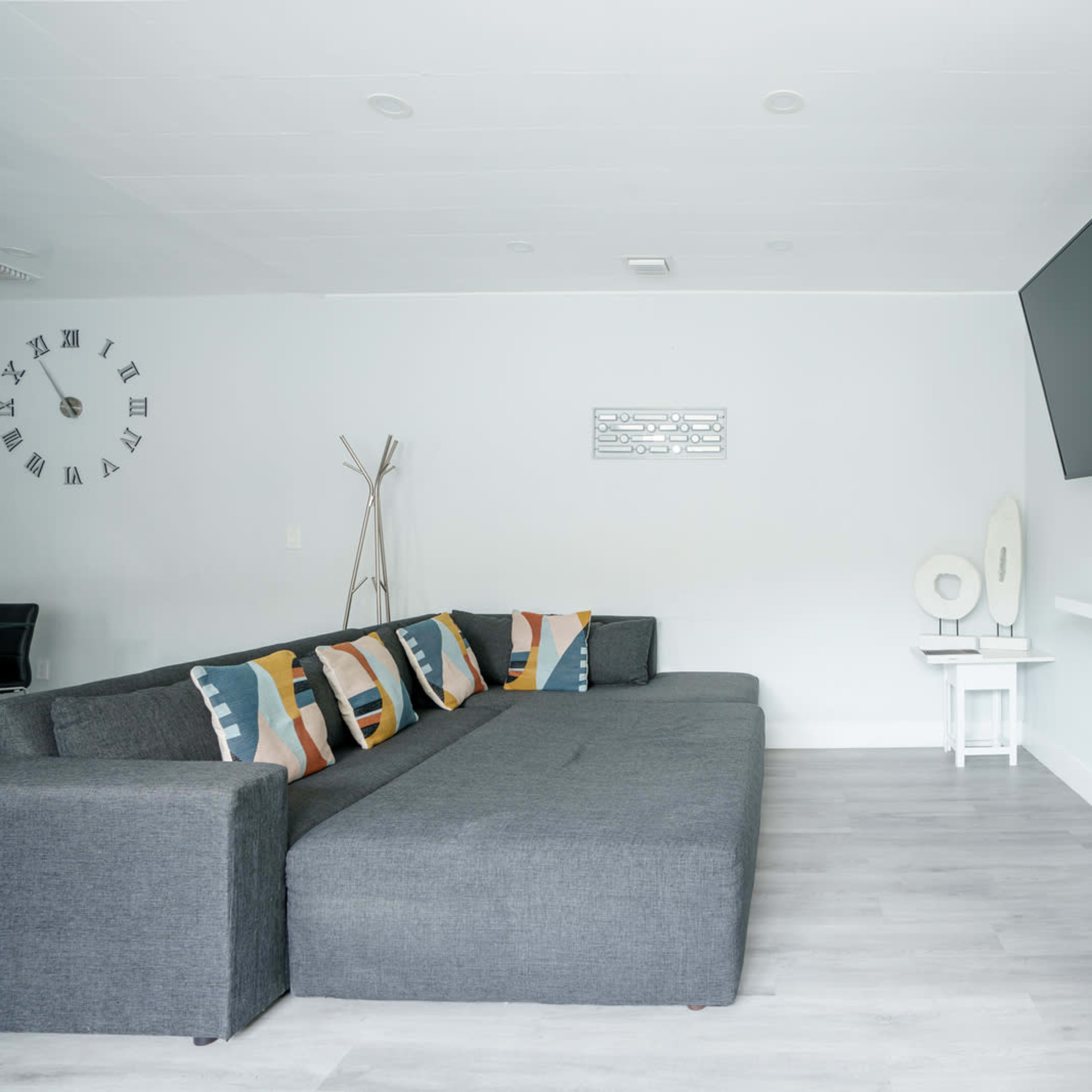 The living room features a gray sectional sofa, a mounted television, a small white side table, and a potted plant in the corner.
