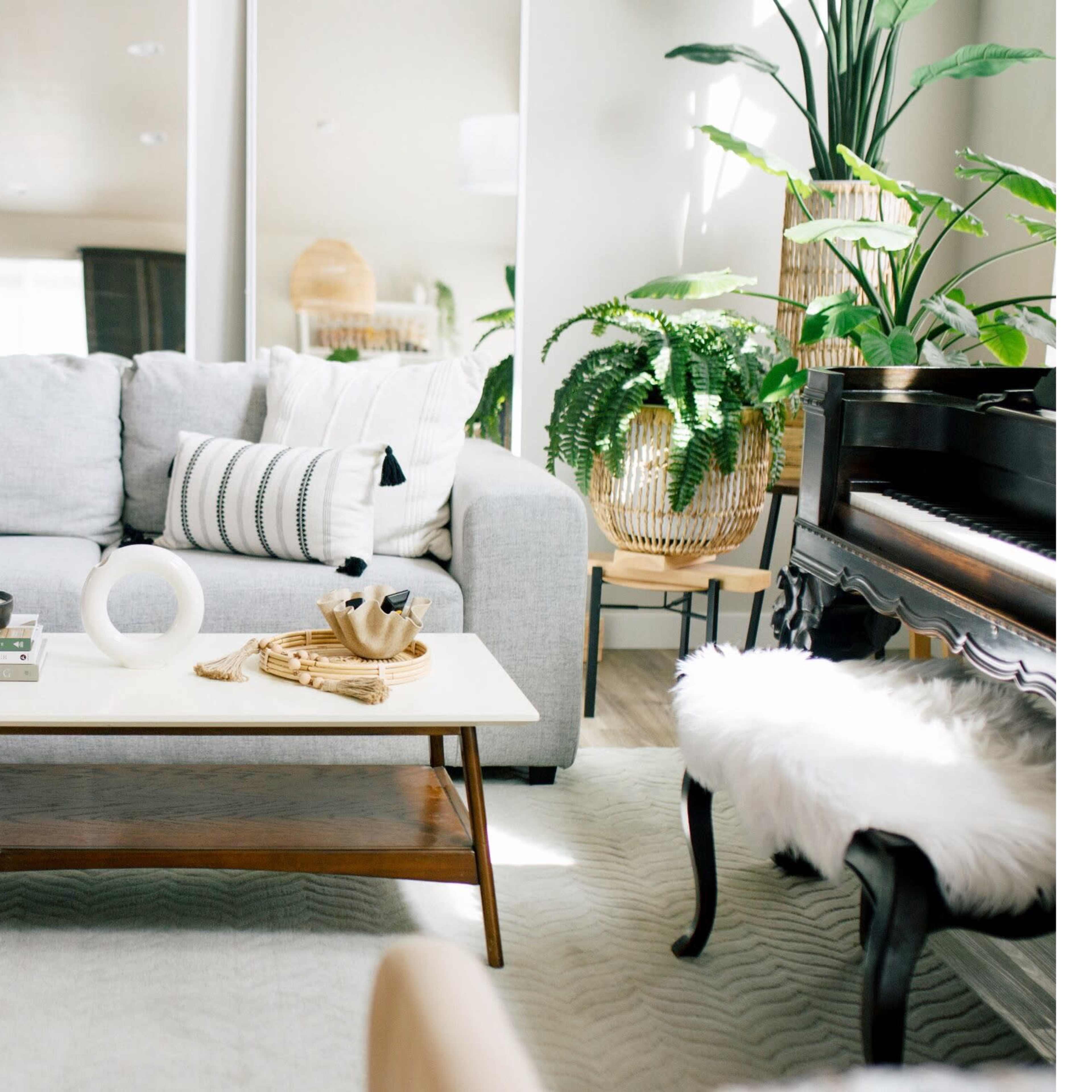 A modern living room featuring a gray sectional sofa, a coffee table with decor items, and a piano surrounded by plants.