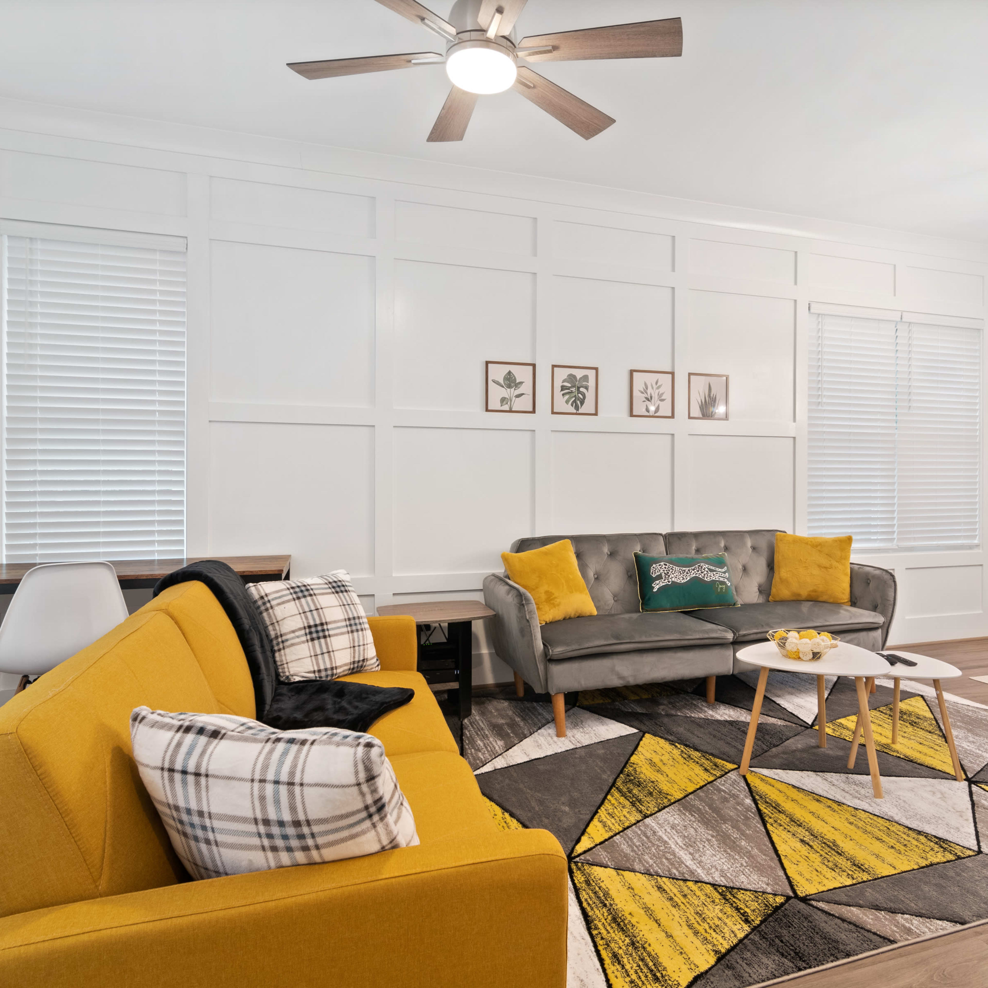 The living area features a gray sofa, a yellow accent chair, a patterned rug, and a dining table with modern chairs under a decorative ceiling light.