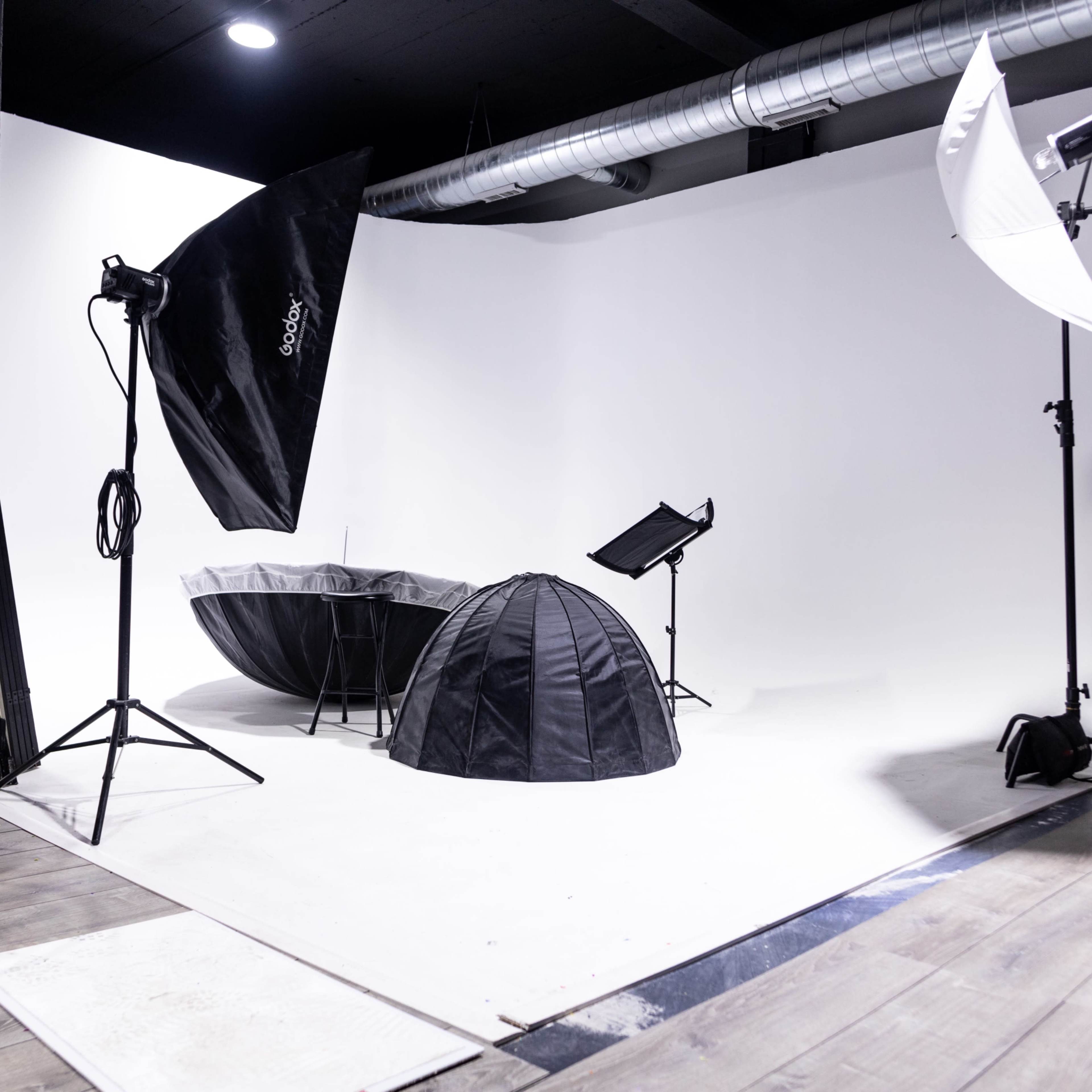 A photography studio setup with a white backdrop, various lighting equipment, and two softboxes positioned on stands.