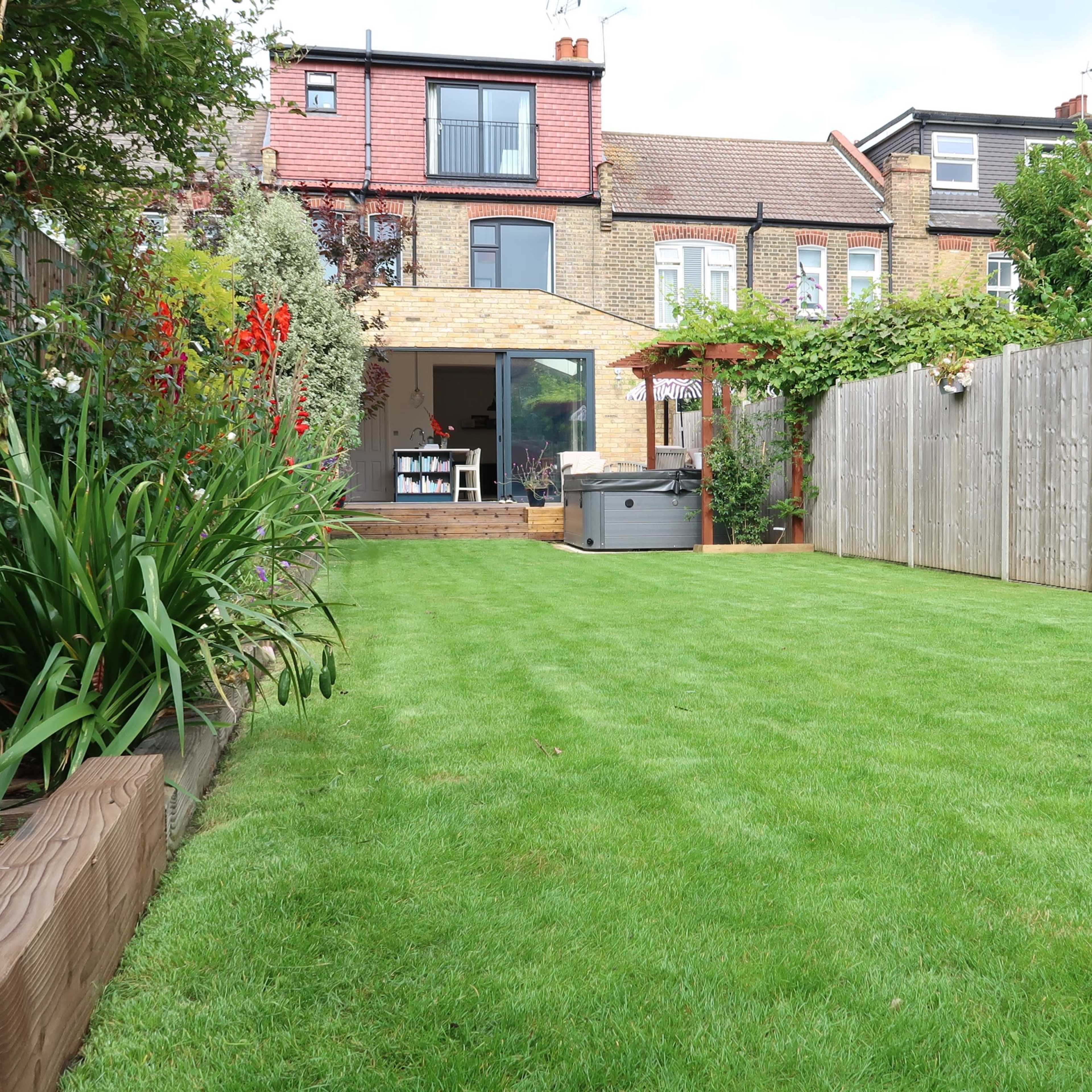 A well-maintained backyard with a lush green lawn, a wooden fence, and a house with a patio in the background.