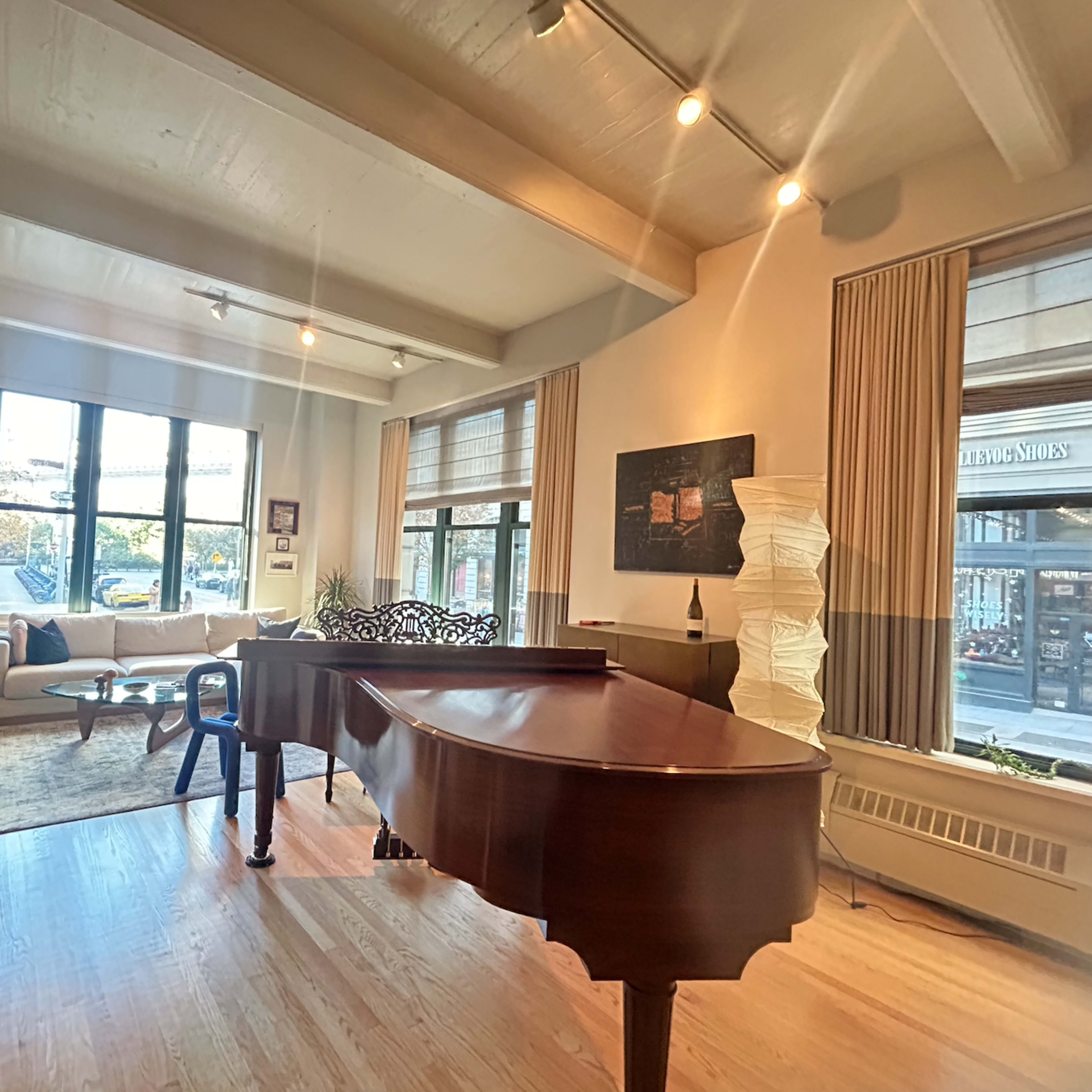 A spacious living room features a grand piano, large windows, a cozy seating area, and a modern decor.