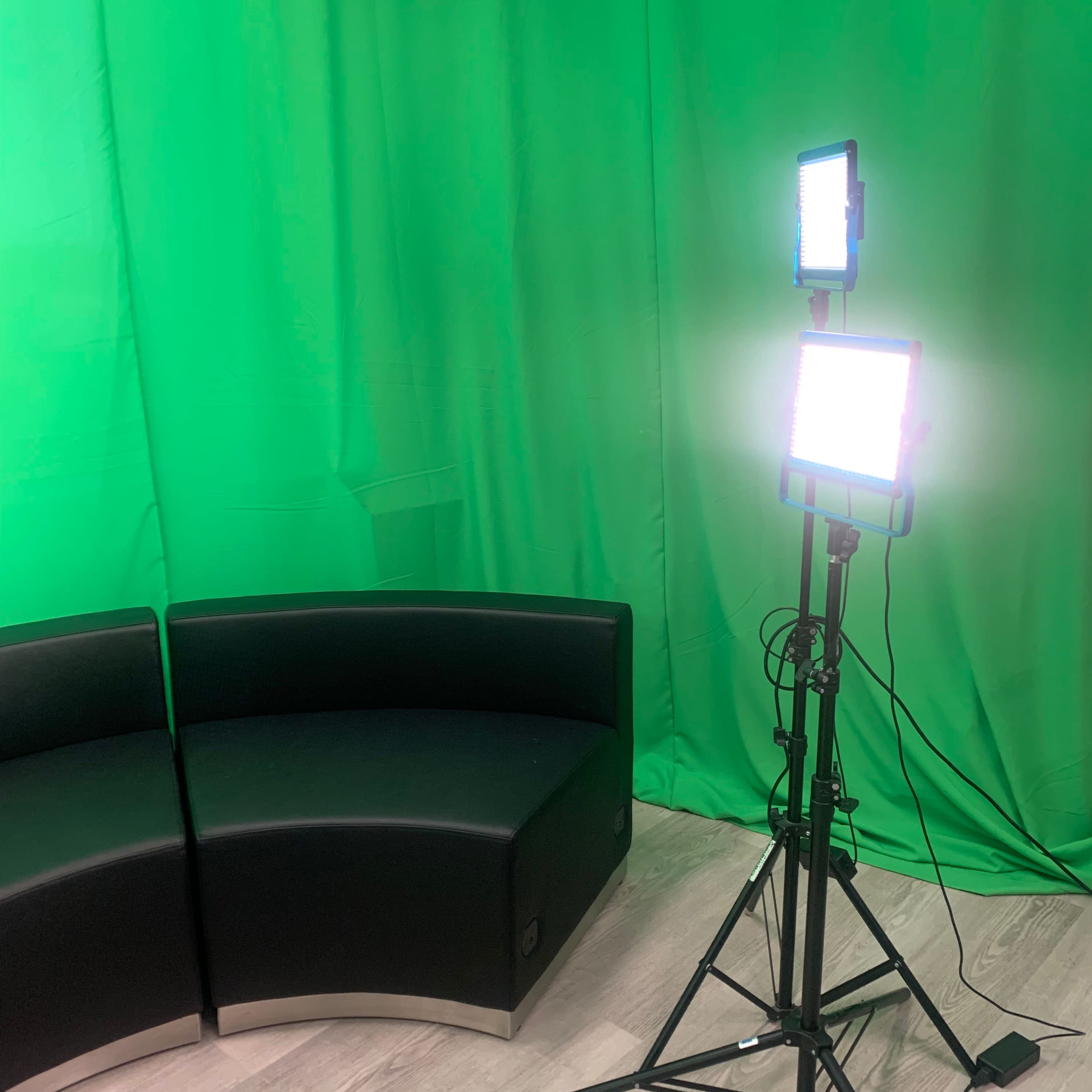 A green backdrop with two lighting panels on stands next to a black curved couch.