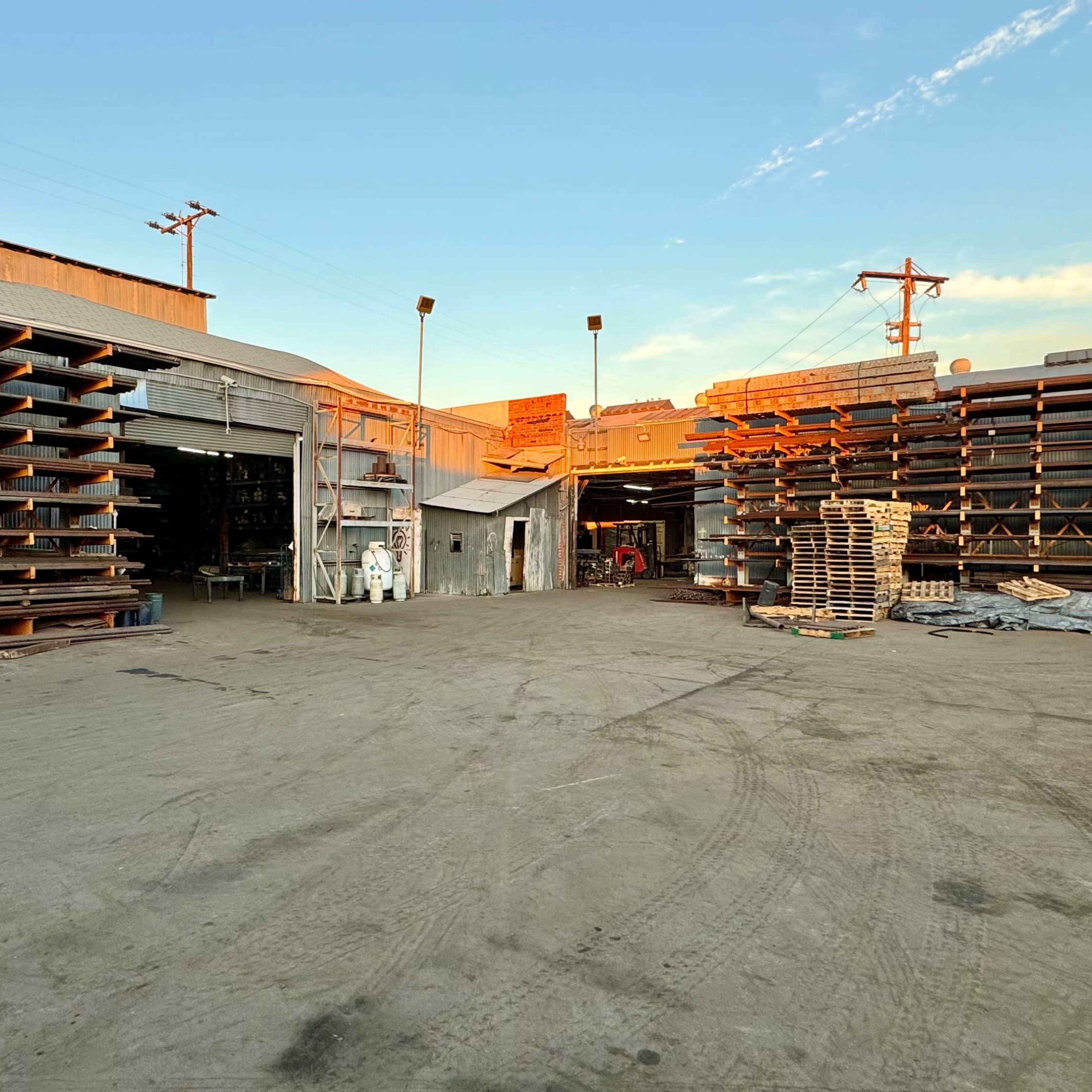 A large industrial yard with stacked materials and open buildings under a clear sky.