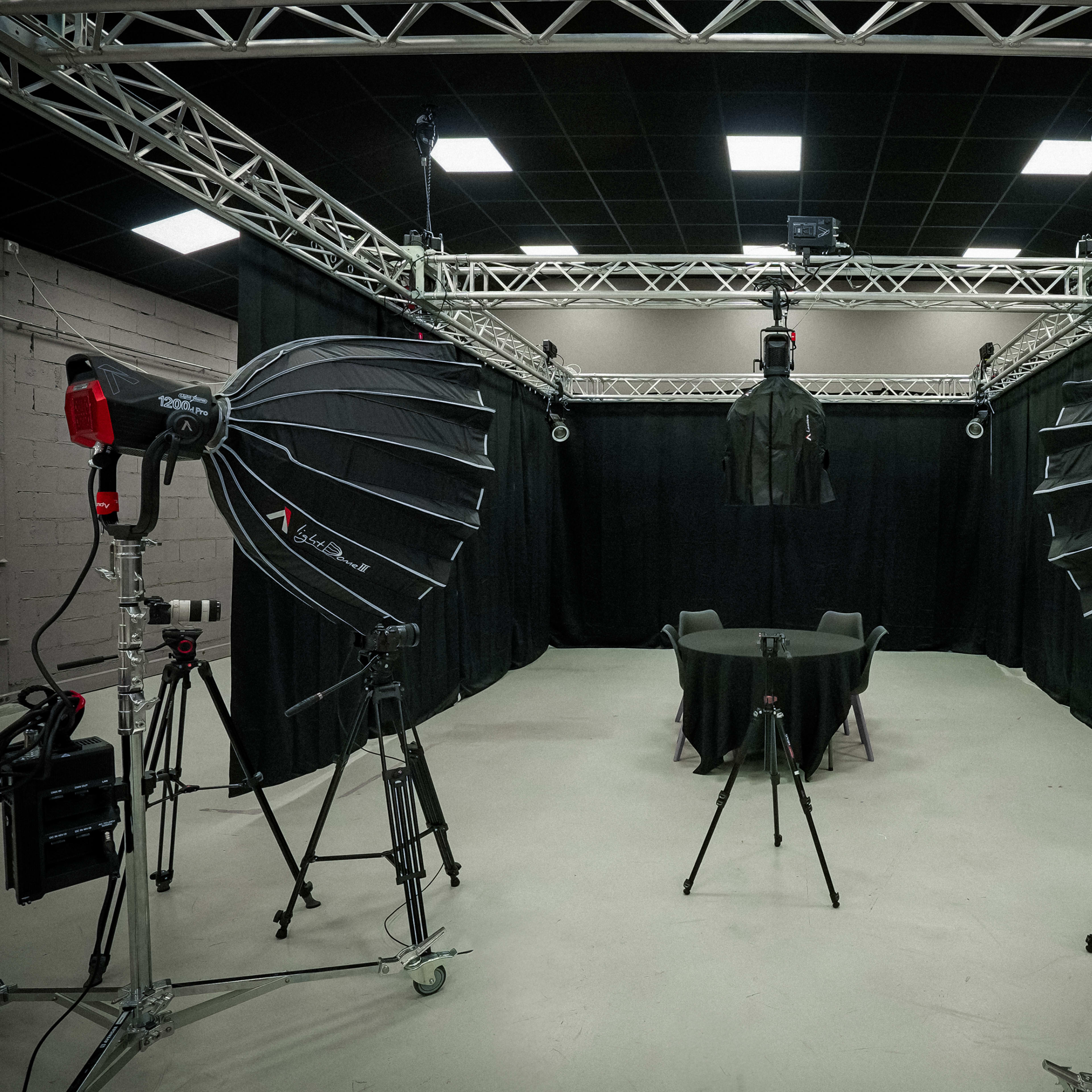 A photography studio equipped with large softbox lights, tripods, and a black backdrop featuring a table and a coat displayed on a hanger.
