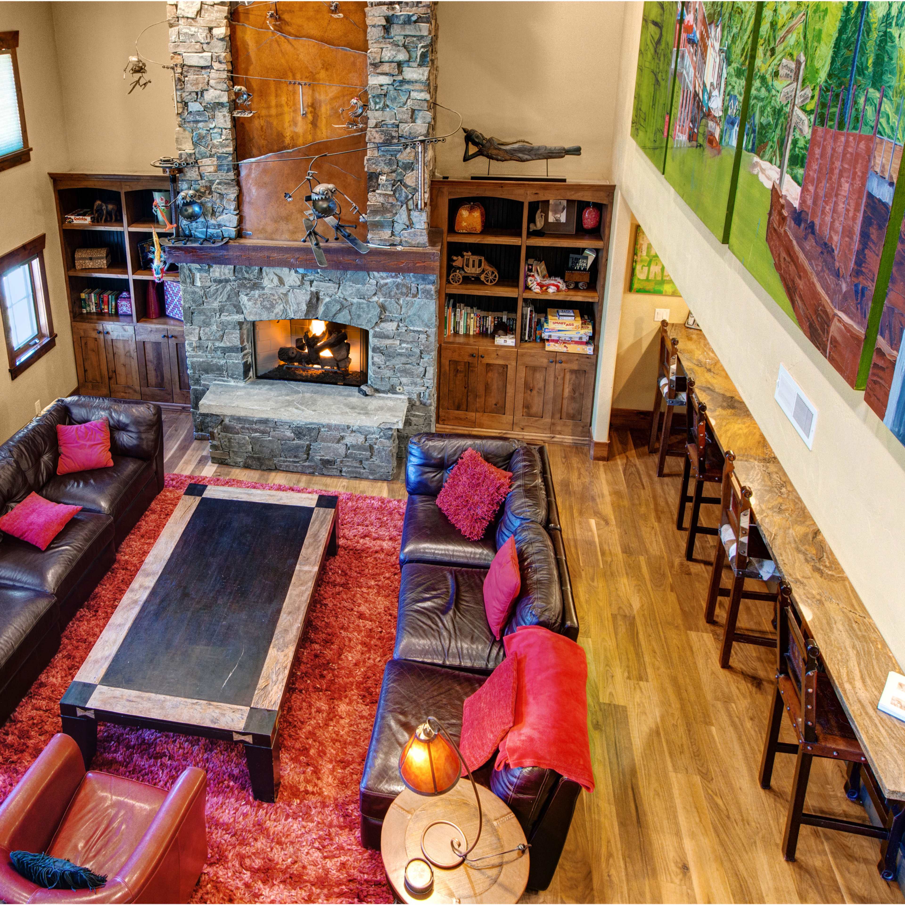 A spacious living room featuring a large stone fireplace, leather sofas arranged around a central coffee table, and a colorful mural on one wall.