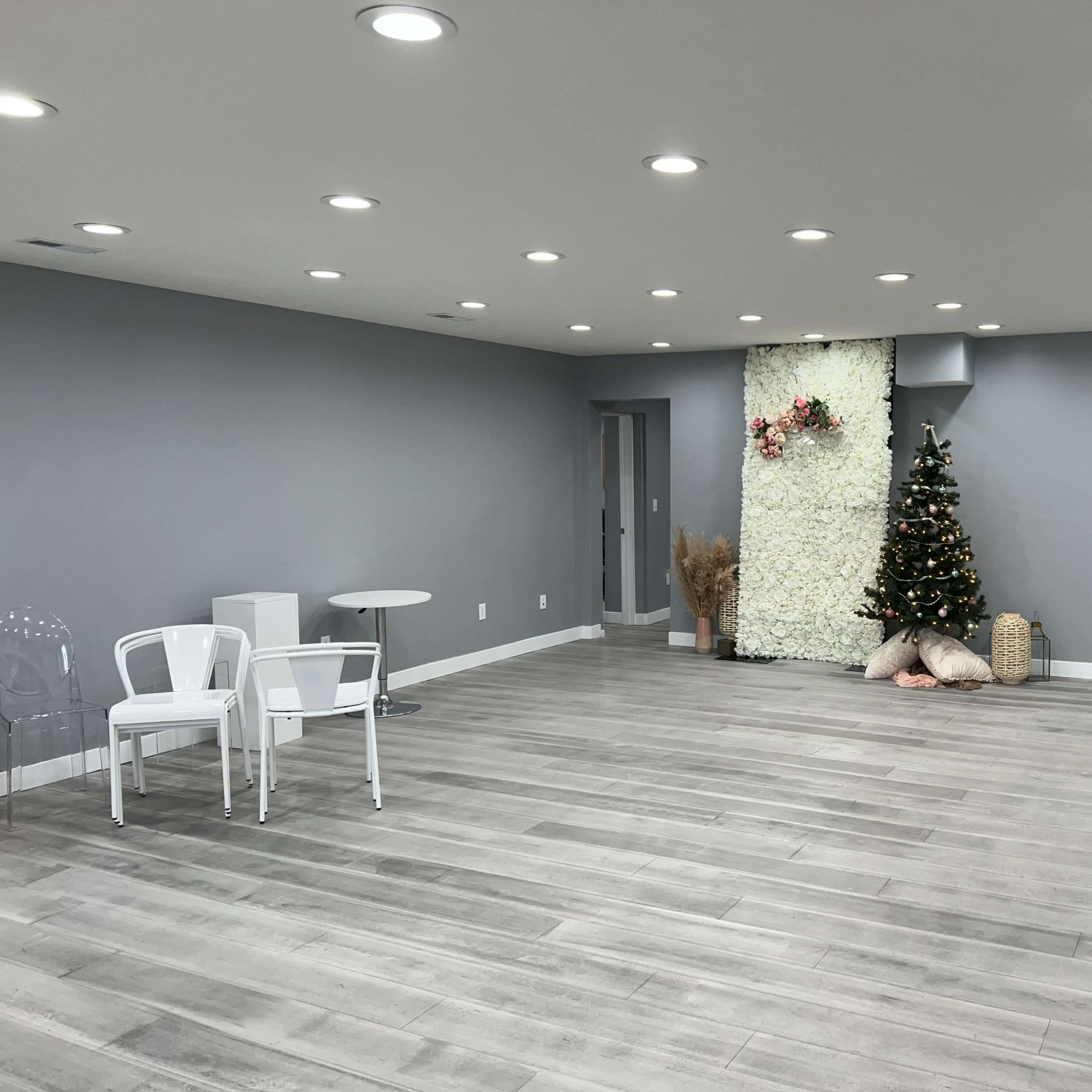 A modern, spacious room with light gray walls, wooden flooring, a decorative wall featuring floral arrangements, and a Christmas tree in one corner.