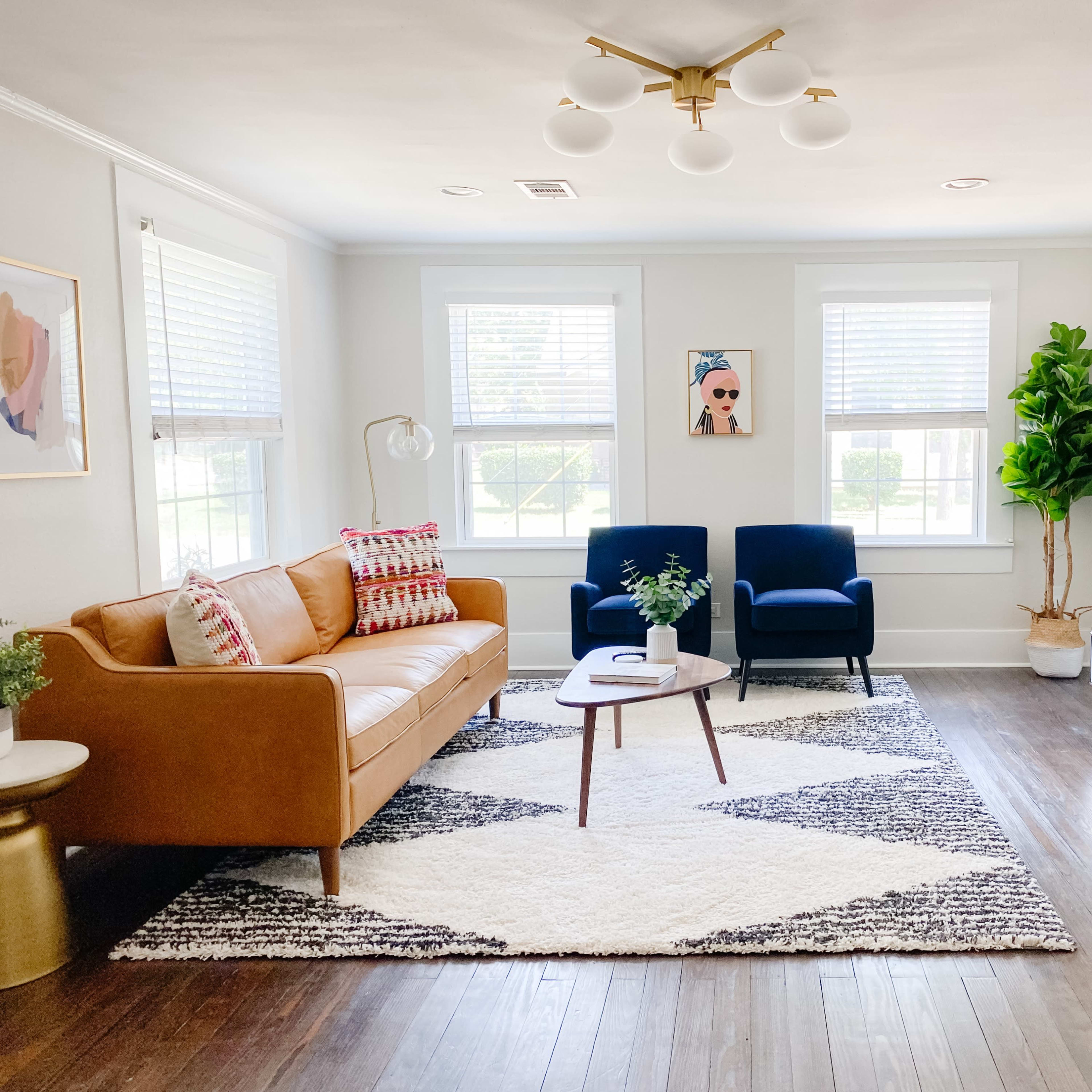 The living room features a tan leather sofa, two blue armchairs, a coffee table, and a patterned rug, illuminated by a modern ceiling light.
