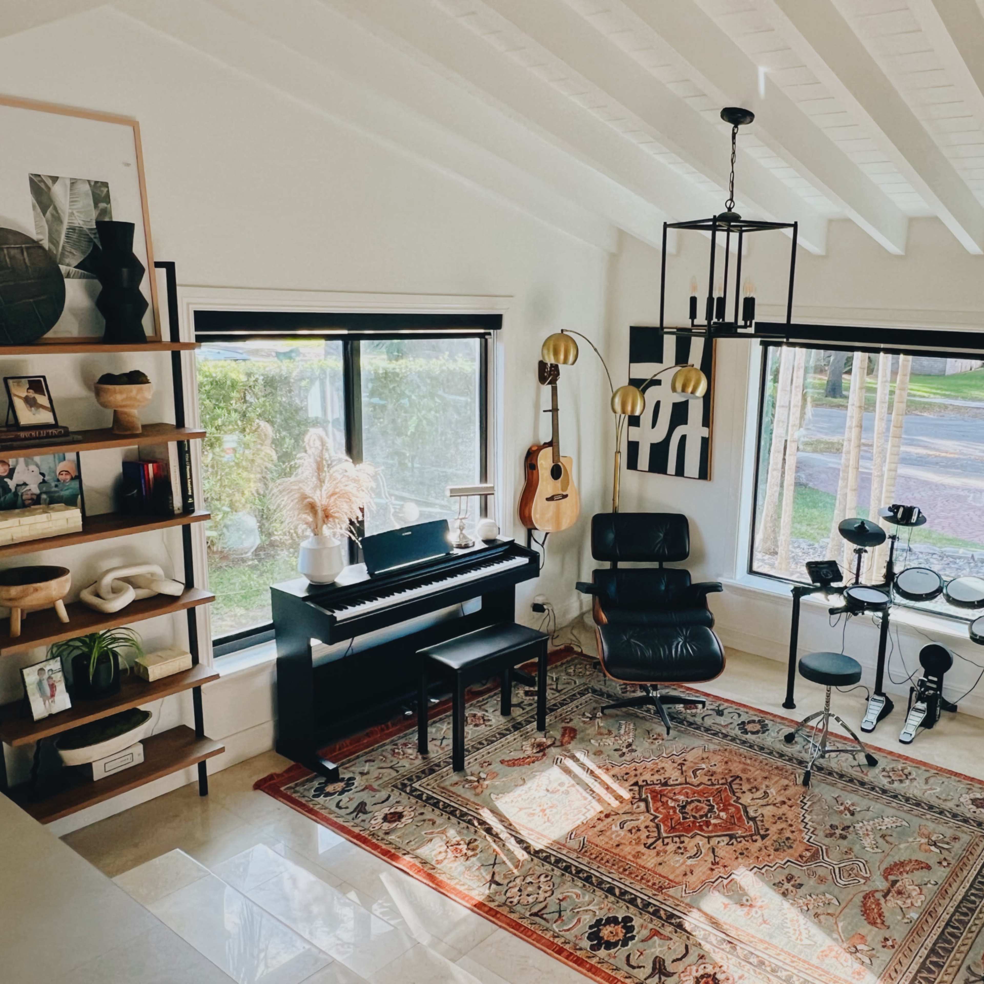 A well-lit room featuring a black piano, an acoustic guitar, a seating area with a black chair, and various decorative items on shelves.