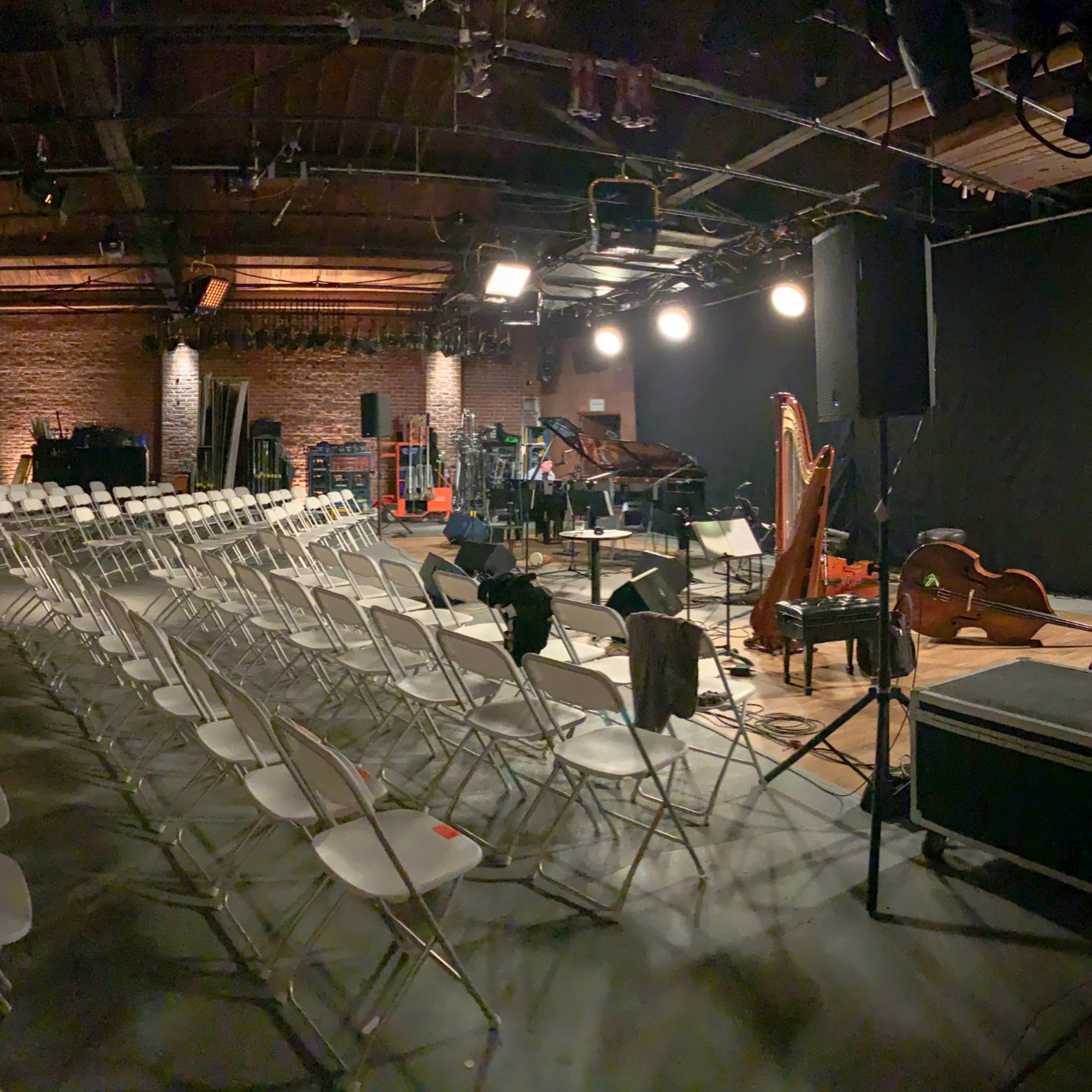 An empty performance space with rows of white chairs arranged facing a stage with musical instruments.