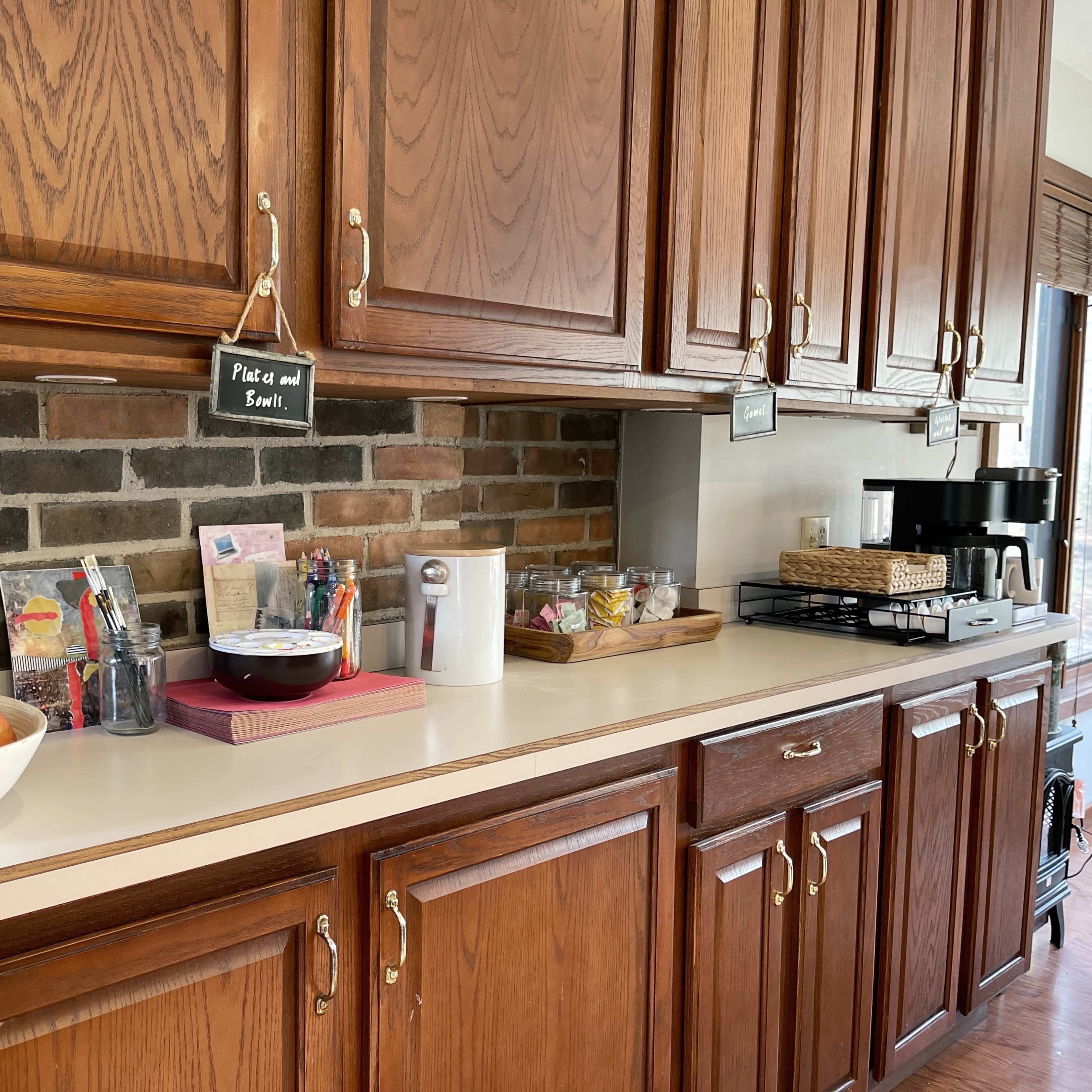 A kitchen with wooden cabinets, a countertop featuring a bowl of apples, a coffee maker, and various kitchen supplies organized on shelves.