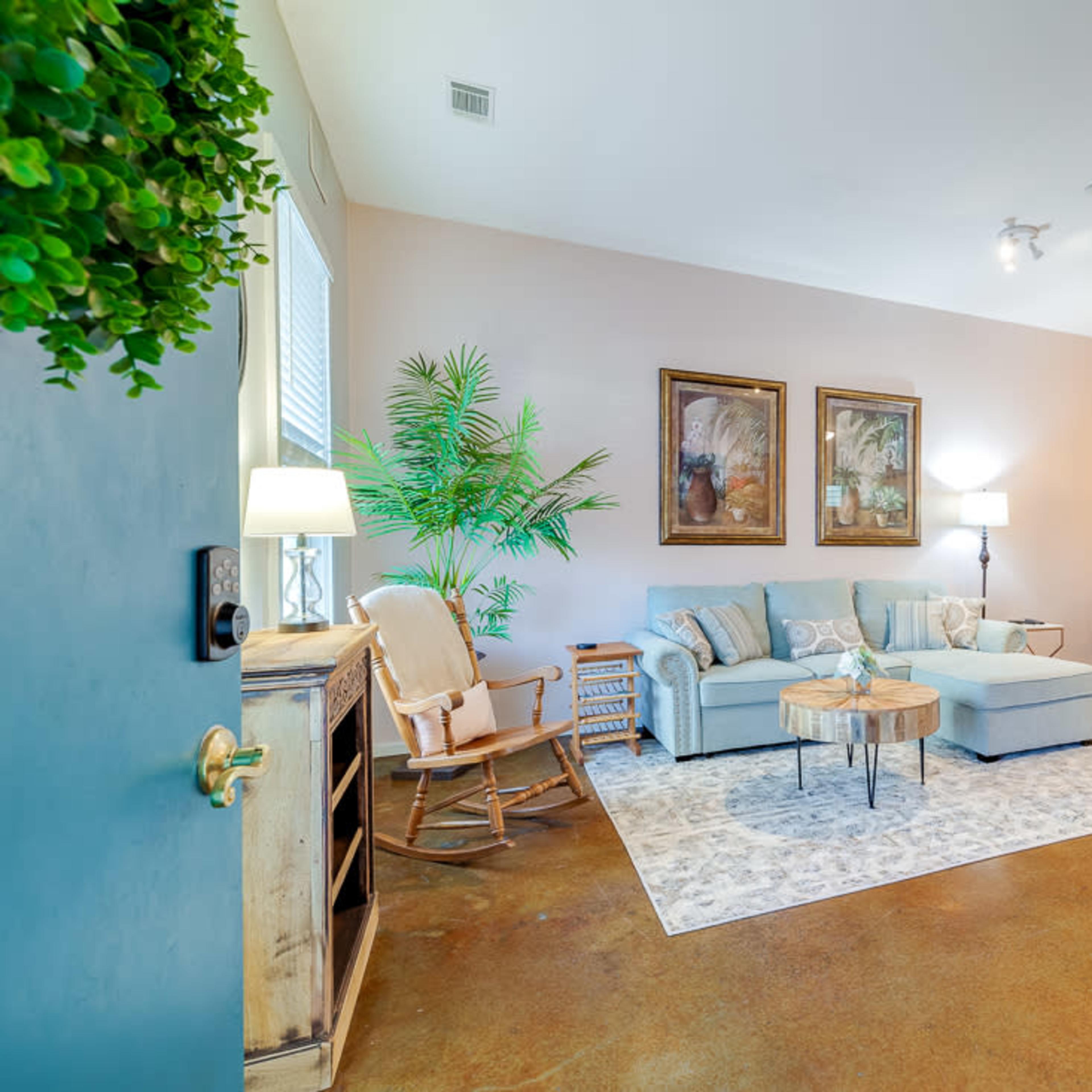 The room features a light blue seating area with a coffee table, a rocking chair, and a dining space with a wooden table and chairs.