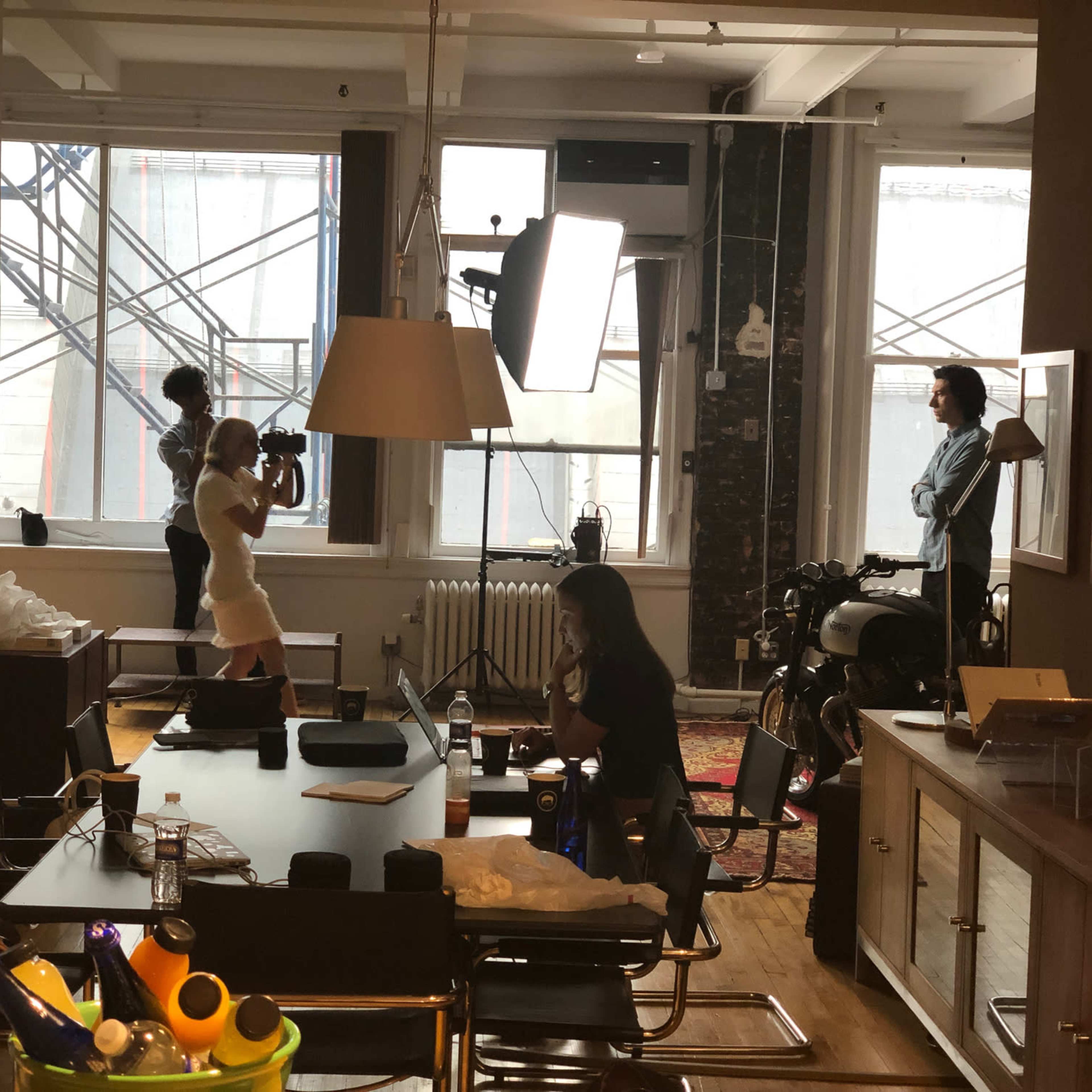 A photography setup in a spacious room with multiple people engaged in a photo shoot, while a motorcycle is parked near a window.