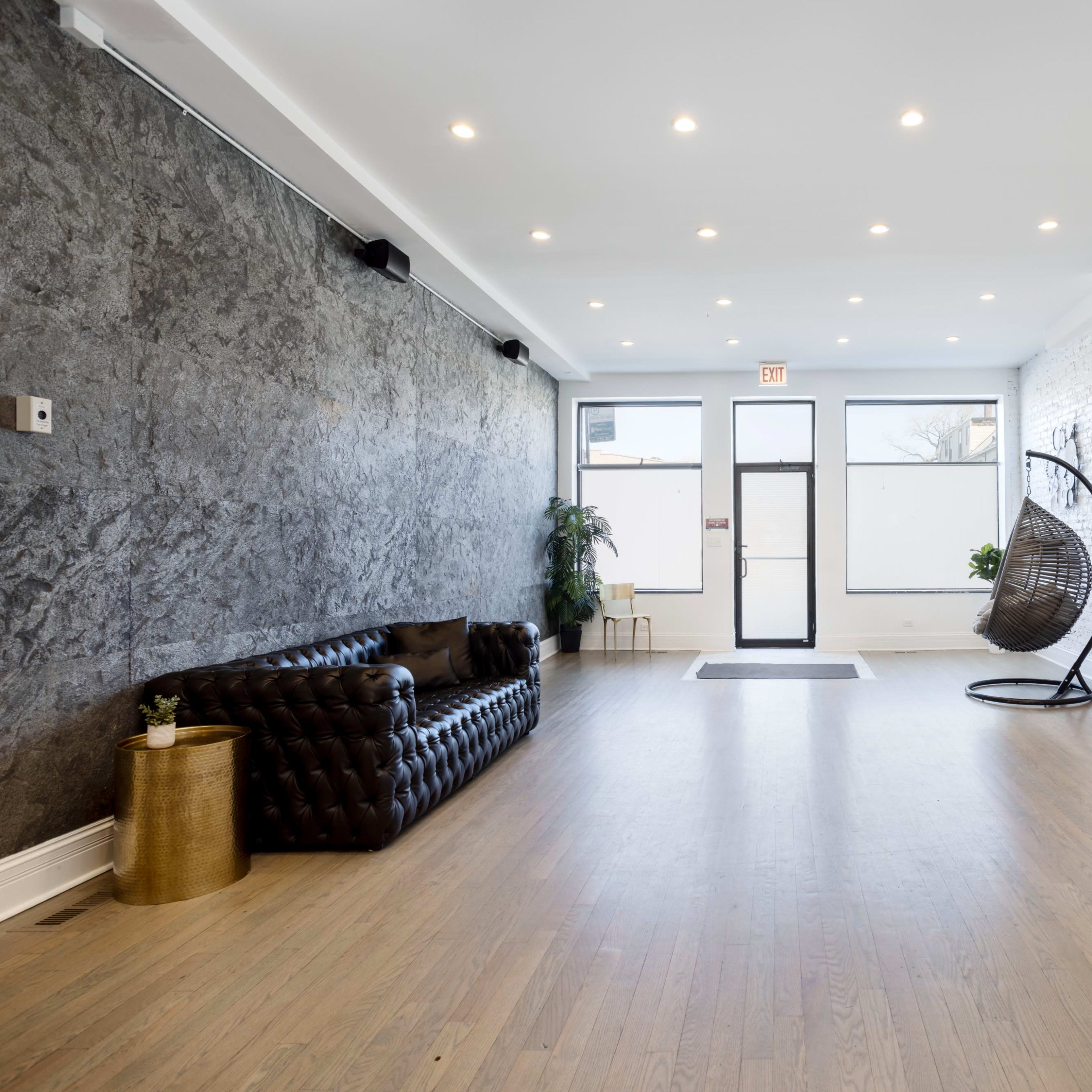 A spacious, modern interior featuring a leather couch, a hanging chair, and large windows allowing natural light to enter.