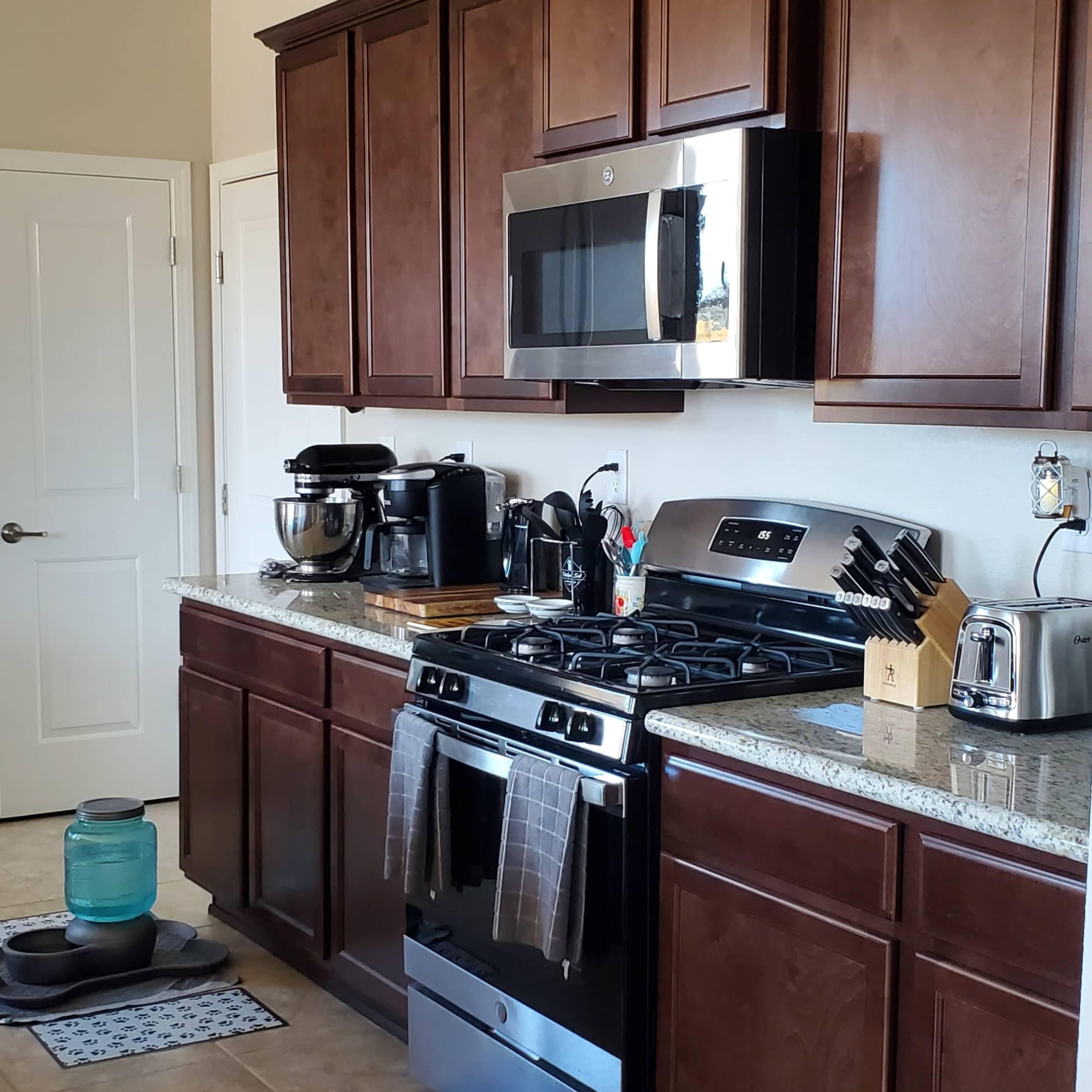 A modern kitchen featuring dark wood cabinetry, a gas stove, a microwave above it, and a variety of kitchen appliances on the countertops.