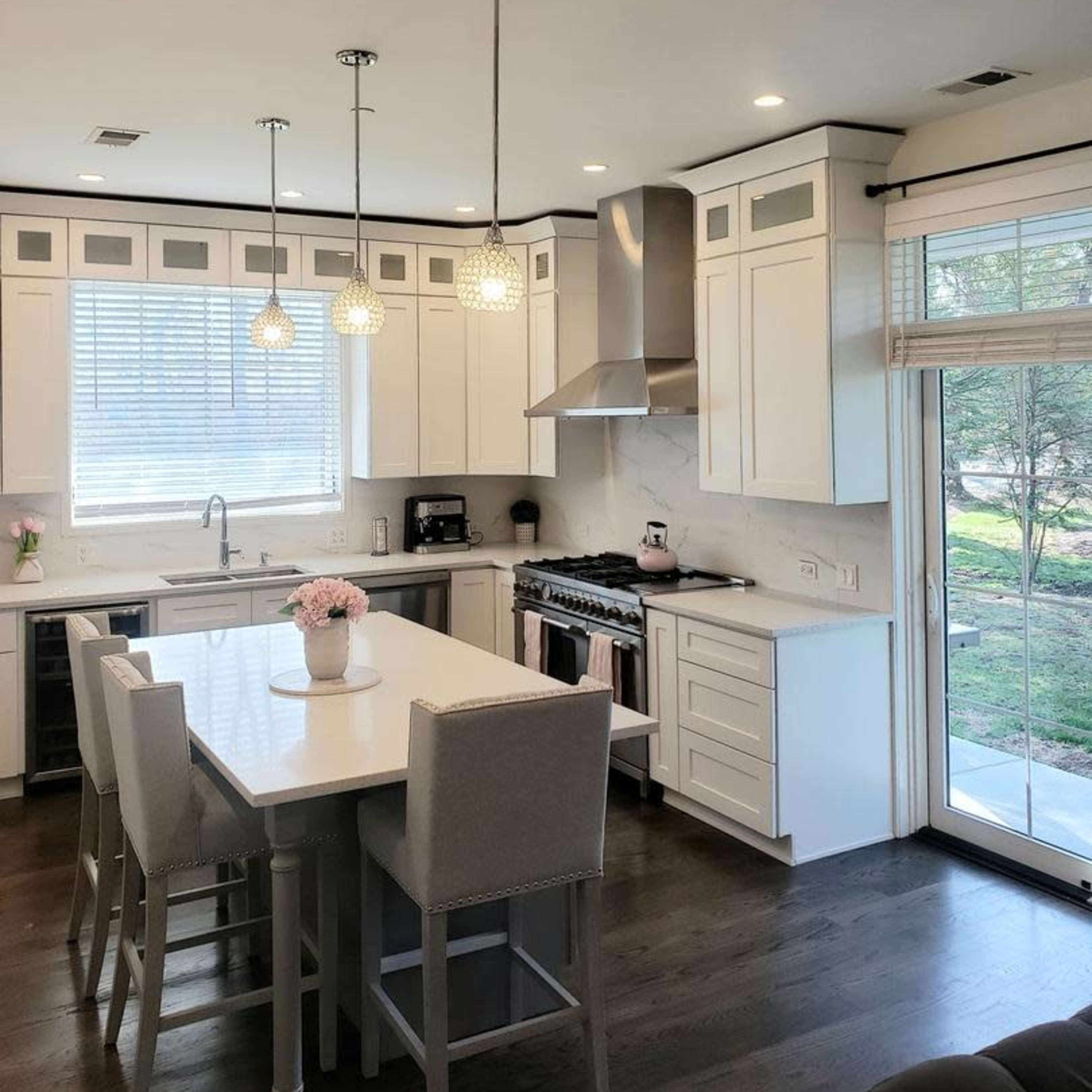 A modern kitchen with white cabinets, a large island with seating, and a view of an outdoor area through sliding glass doors.