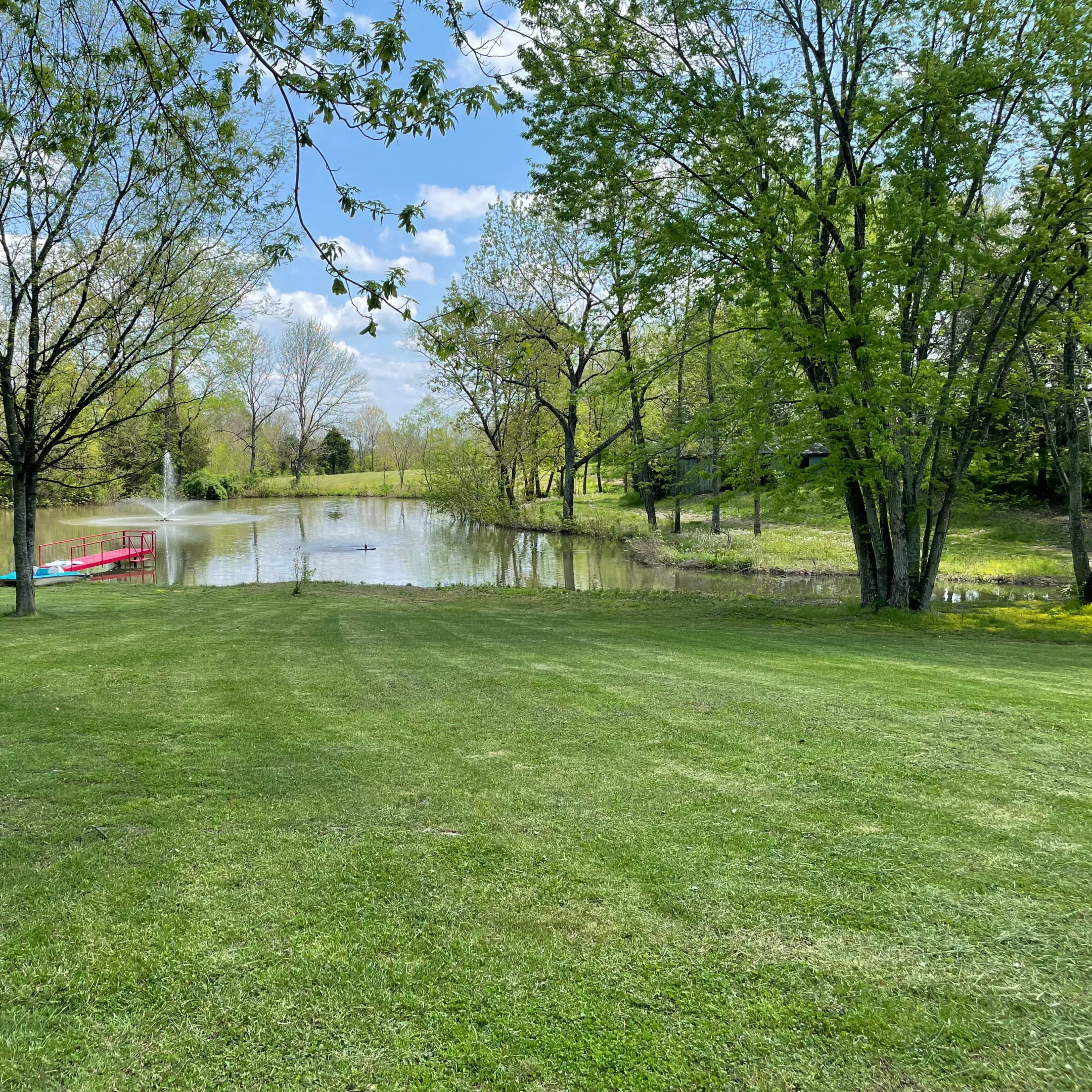 A serene pond surrounded by lush greenery and trees, with a small red canoe on the water's edge.
