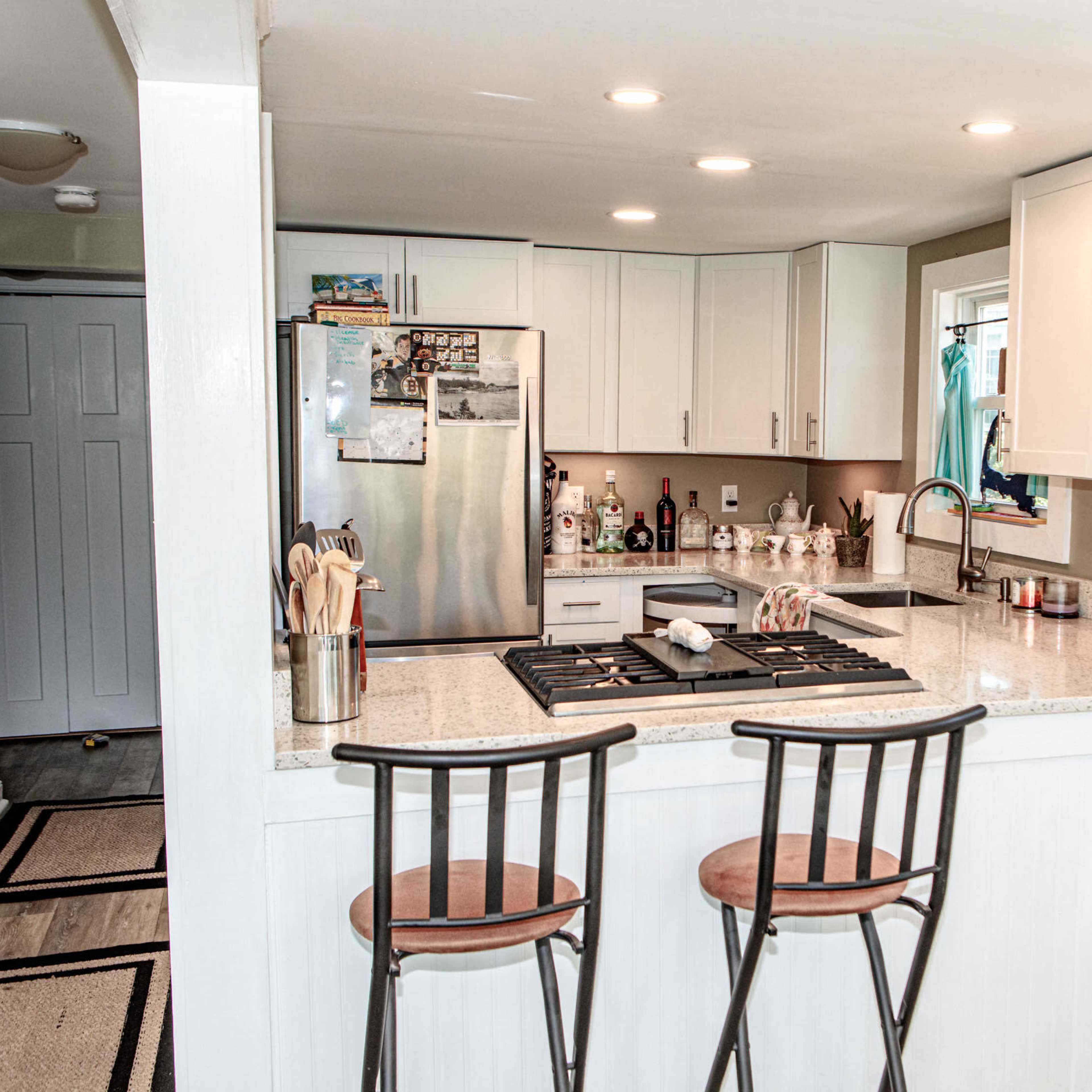 A modern kitchen features a central island with two bar stools, stainless steel appliances, and light-colored cabinetry.