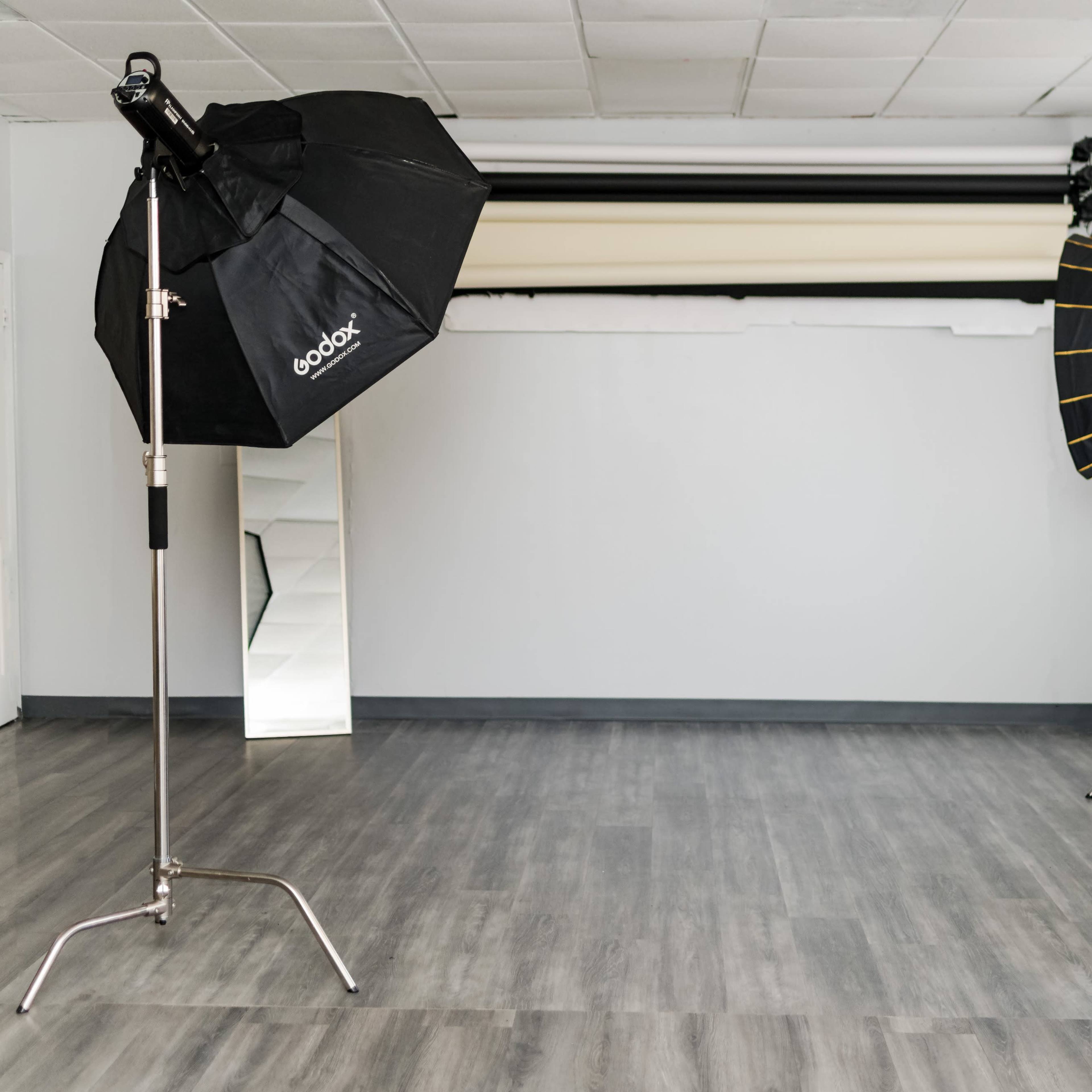 A spacious photography studio equipped with two light stands and a backdrop system, featuring a mirror and a potted plant in the corner.