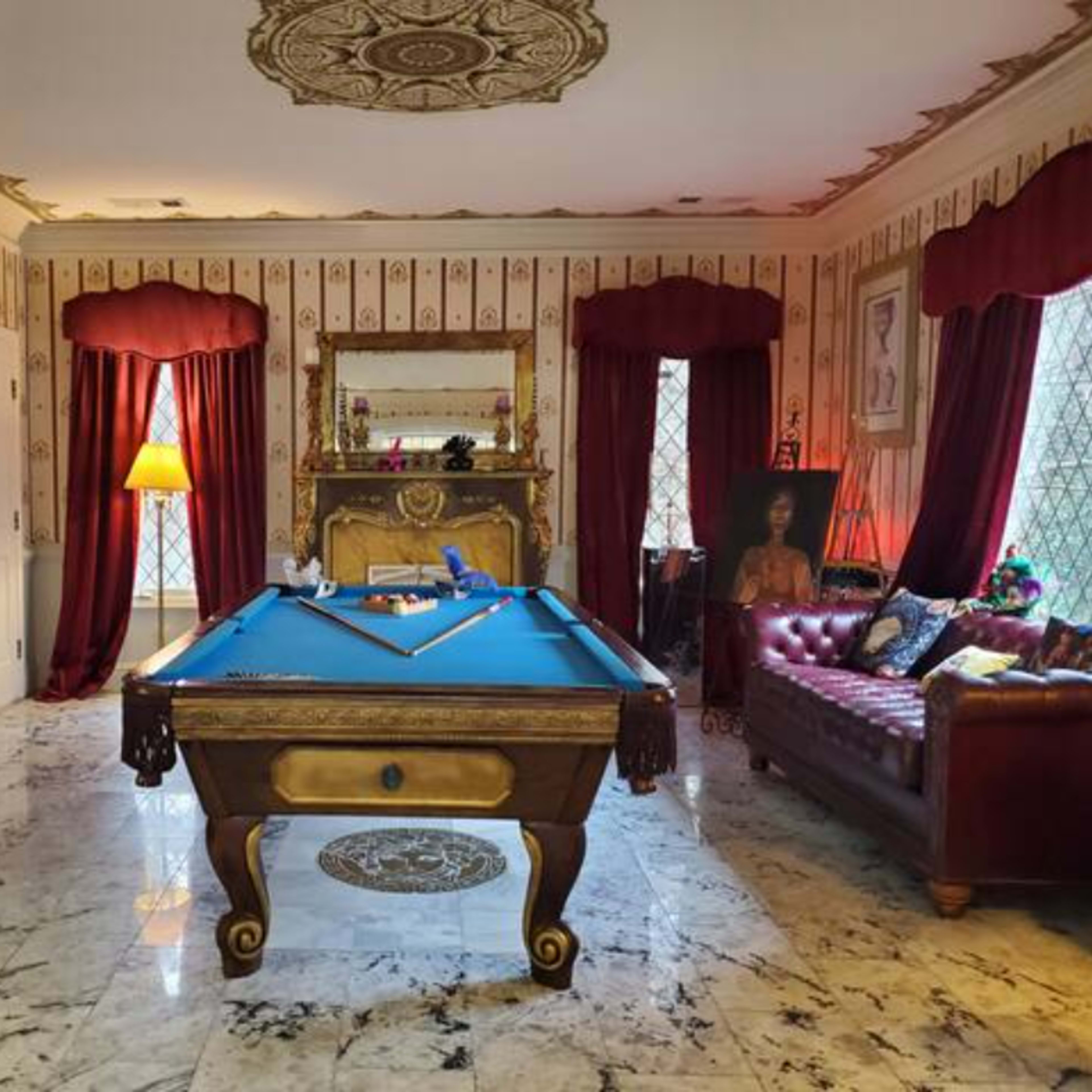 The room features a billiard table at its center, surrounded by ornate decor, patterned wallpaper, and elegant furniture, including a leather sofa and a decorative mirror.