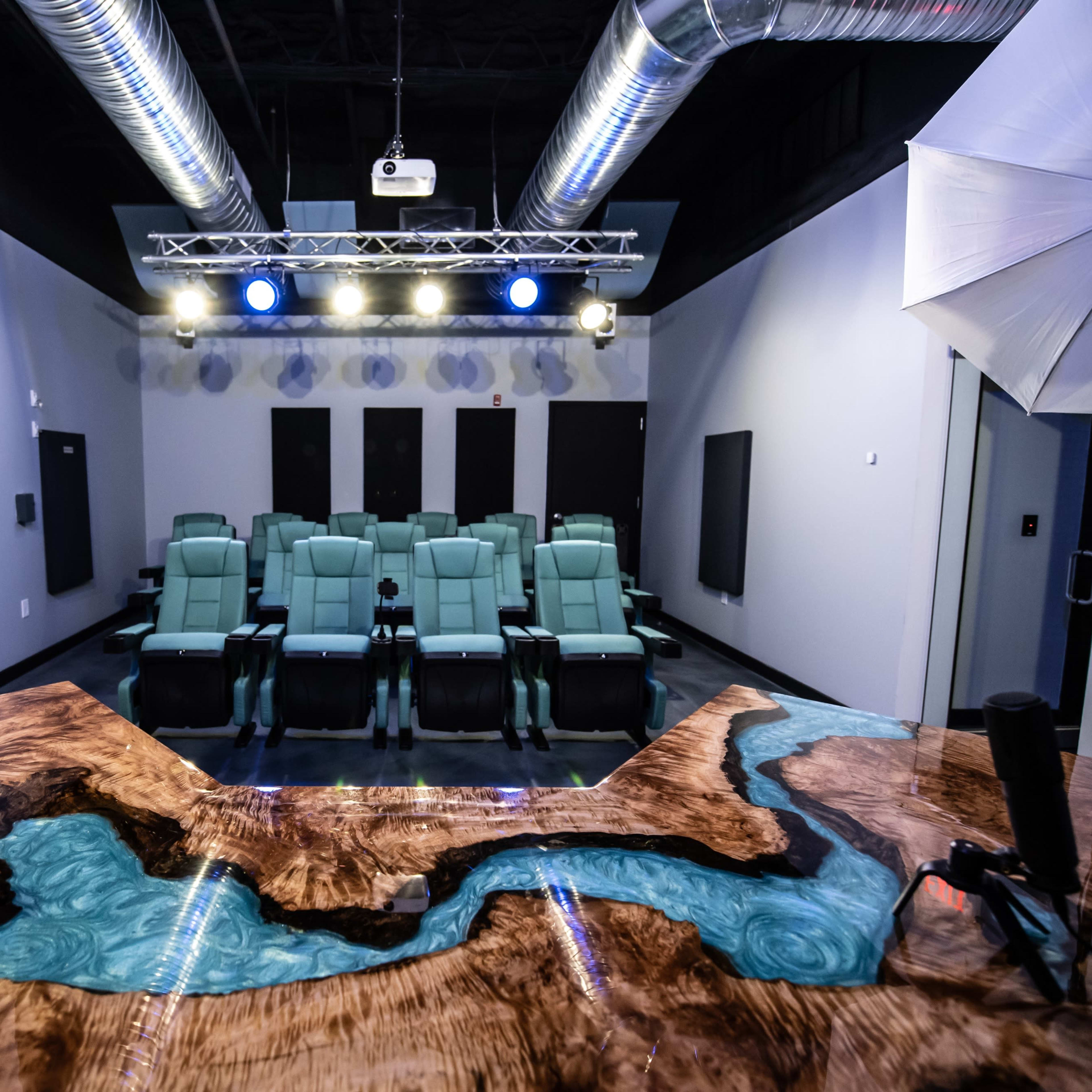A modern home theater setup with green reclining seats facing a projector screen, and professional lighting equipment positioned above.
