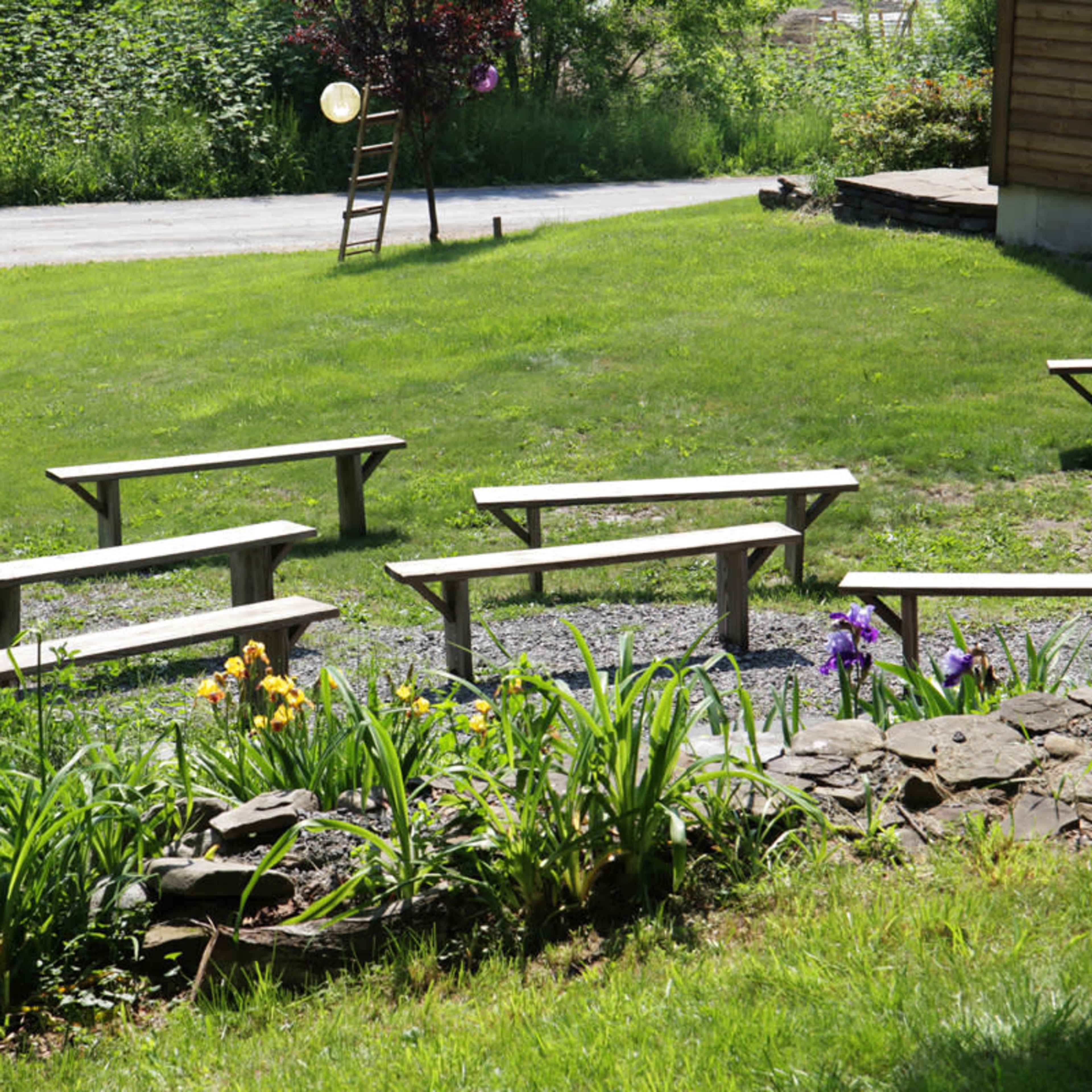 A grassy area with wooden benches arranged in a semi-circle and a flowerbed featuring blooming plants nearby.