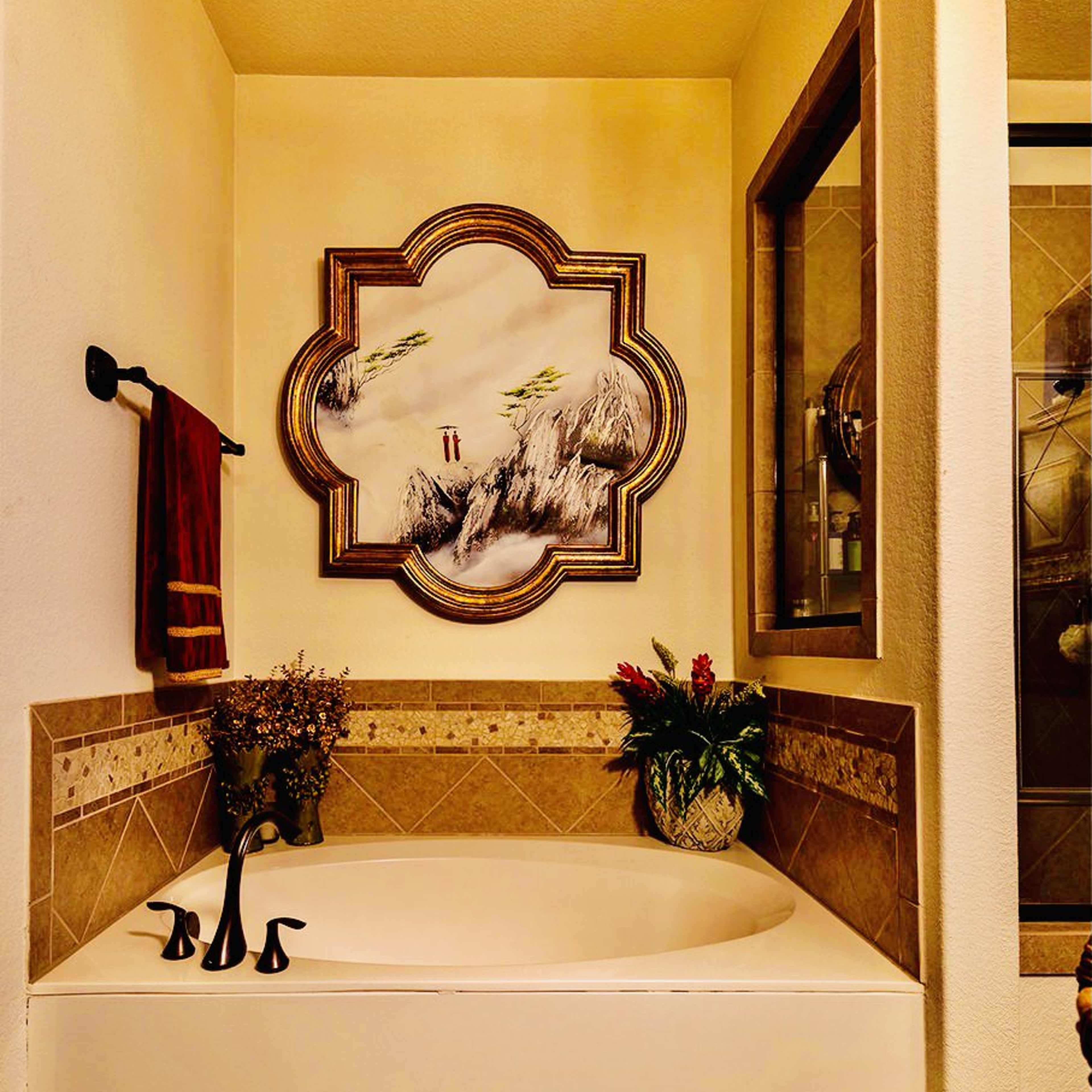 A bathroom featuring a freestanding bathtub, a decorative wall painting, and a vase with flowers on a countertop.
